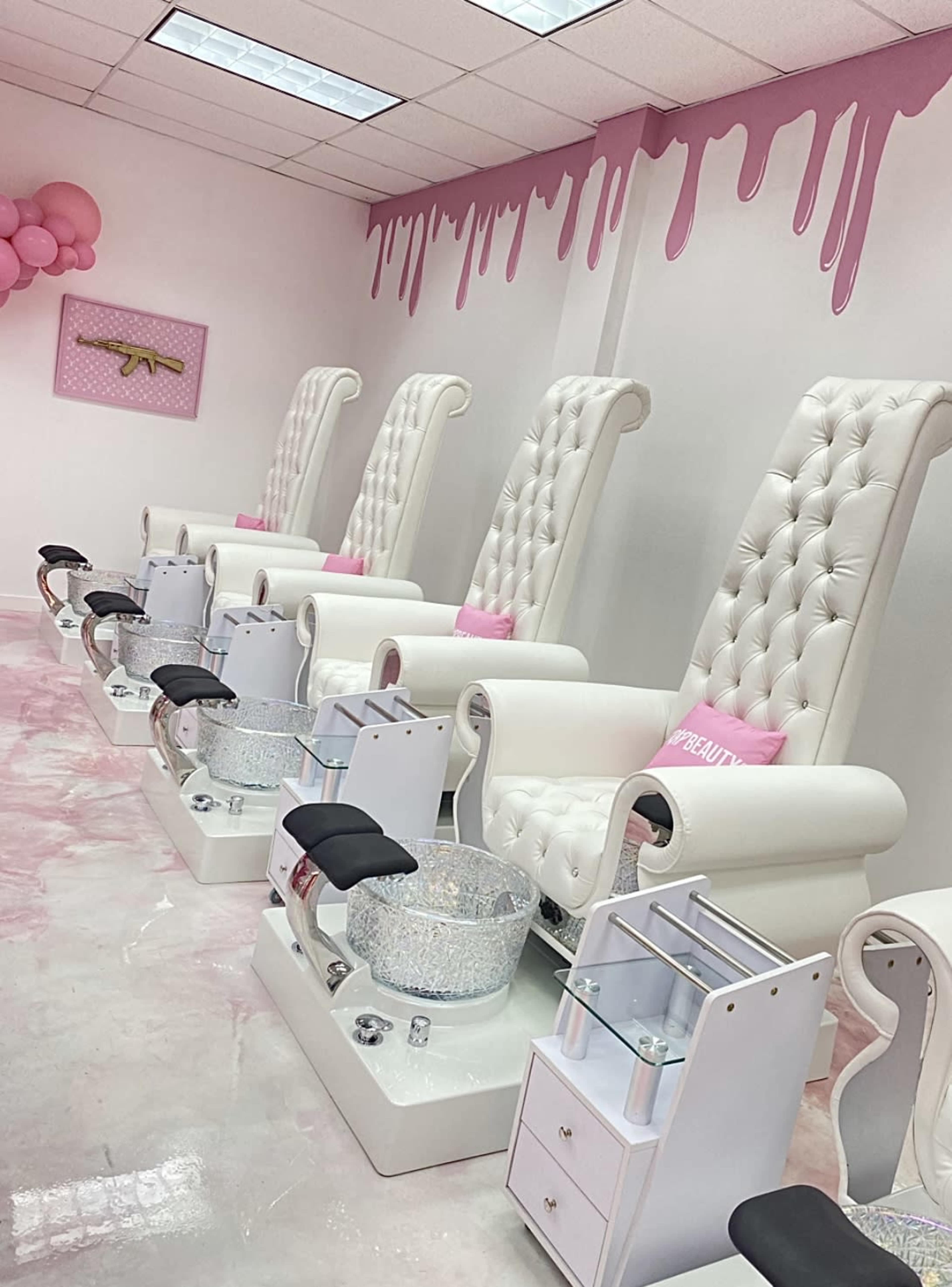 A nail salon interior with several white tufted chairs arranged in a row, each with a sparkling manicure bowl and a small side table.