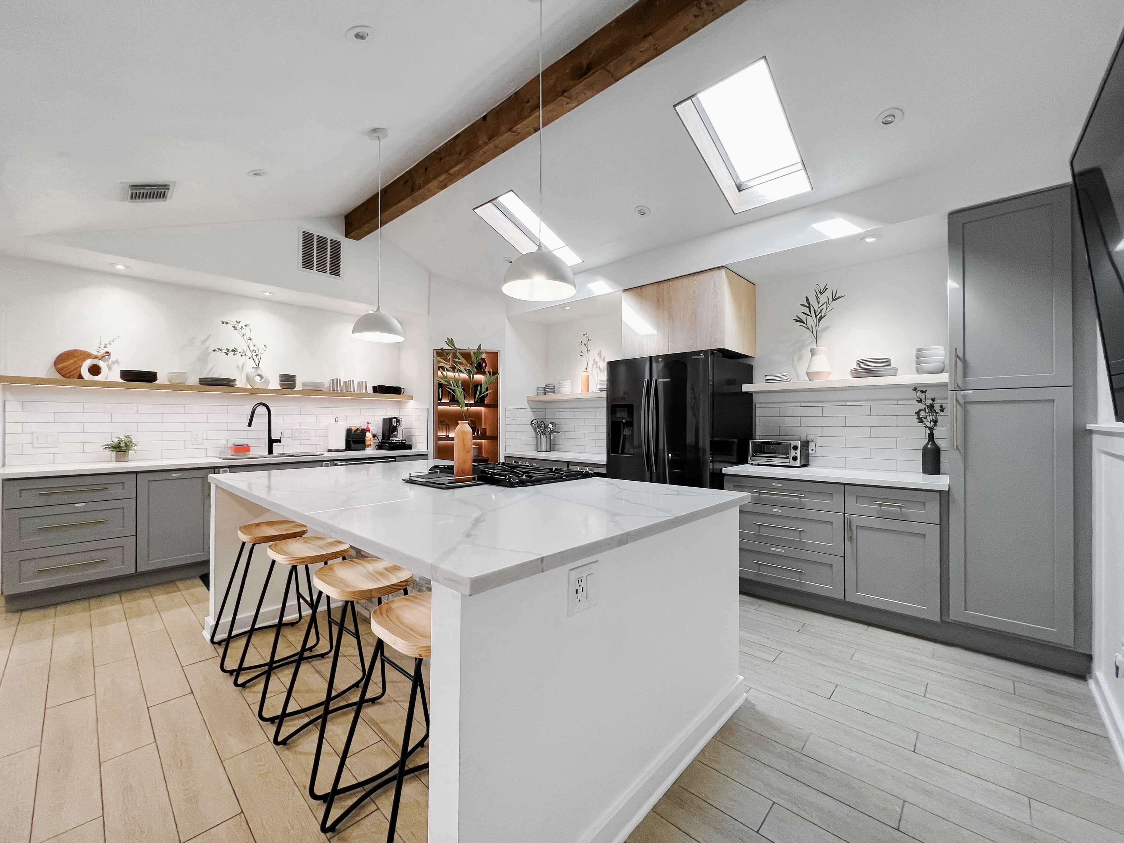 The kitchen features a central island with bar stools, gray cabinetry, white countertops, and modern appliances.