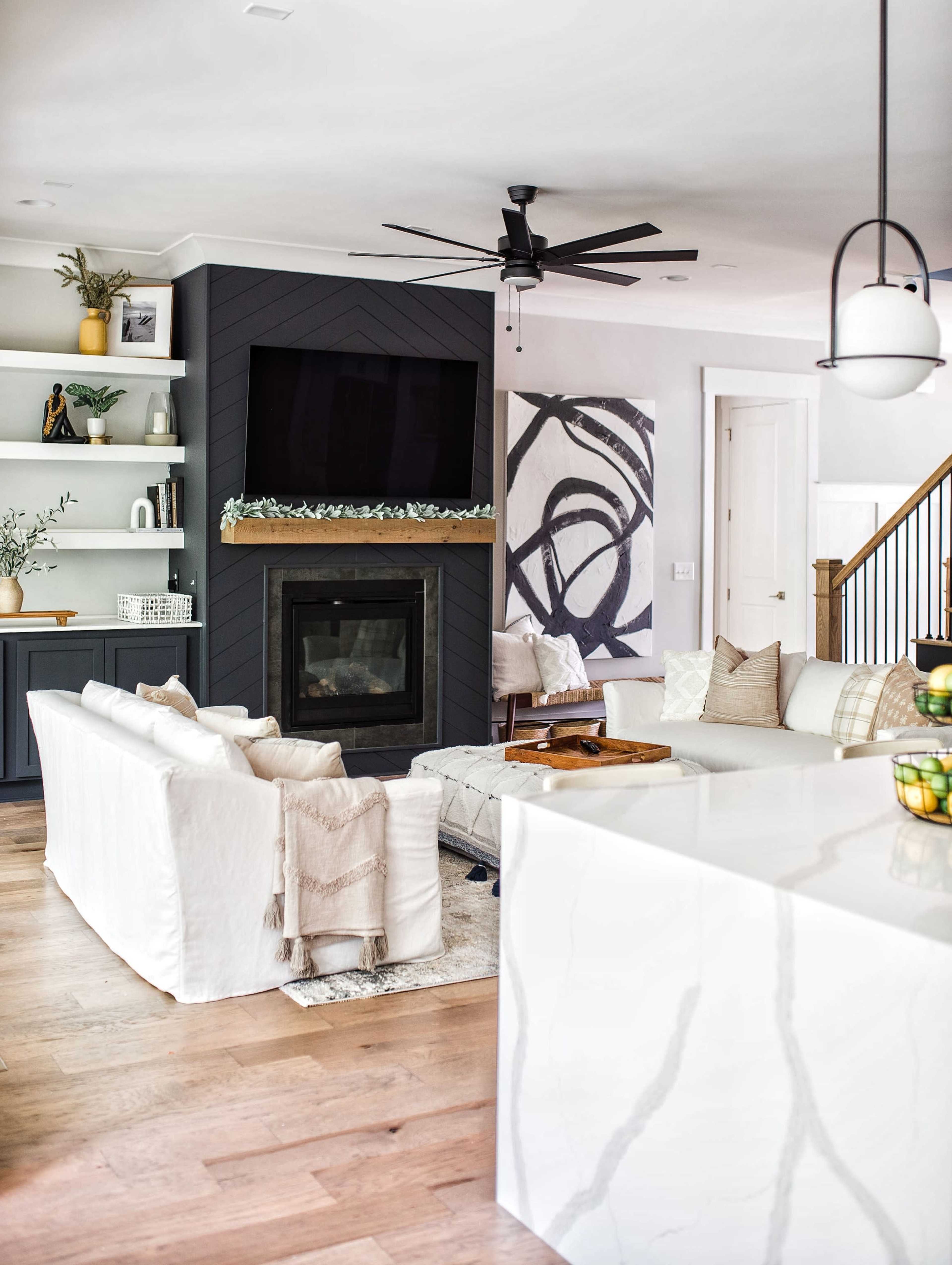 A modern living room features a white couch, a dark gray accent wall with a television, a simple fireplace, and light wood flooring.