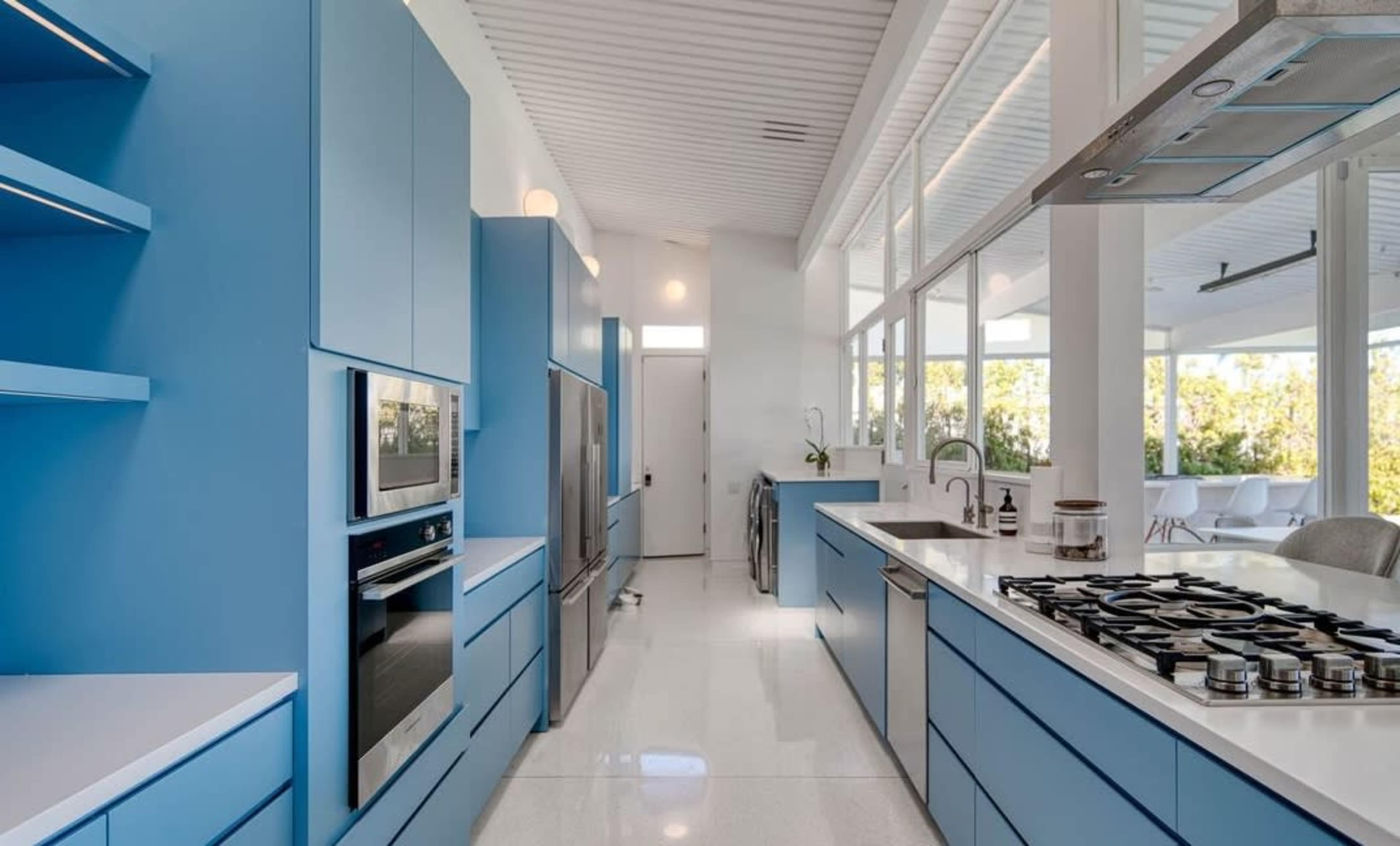 A modern kitchen features blue cabinetry, stainless steel appliances, and a large island with a gas stovetop, all set under a bright, airy atmosphere.