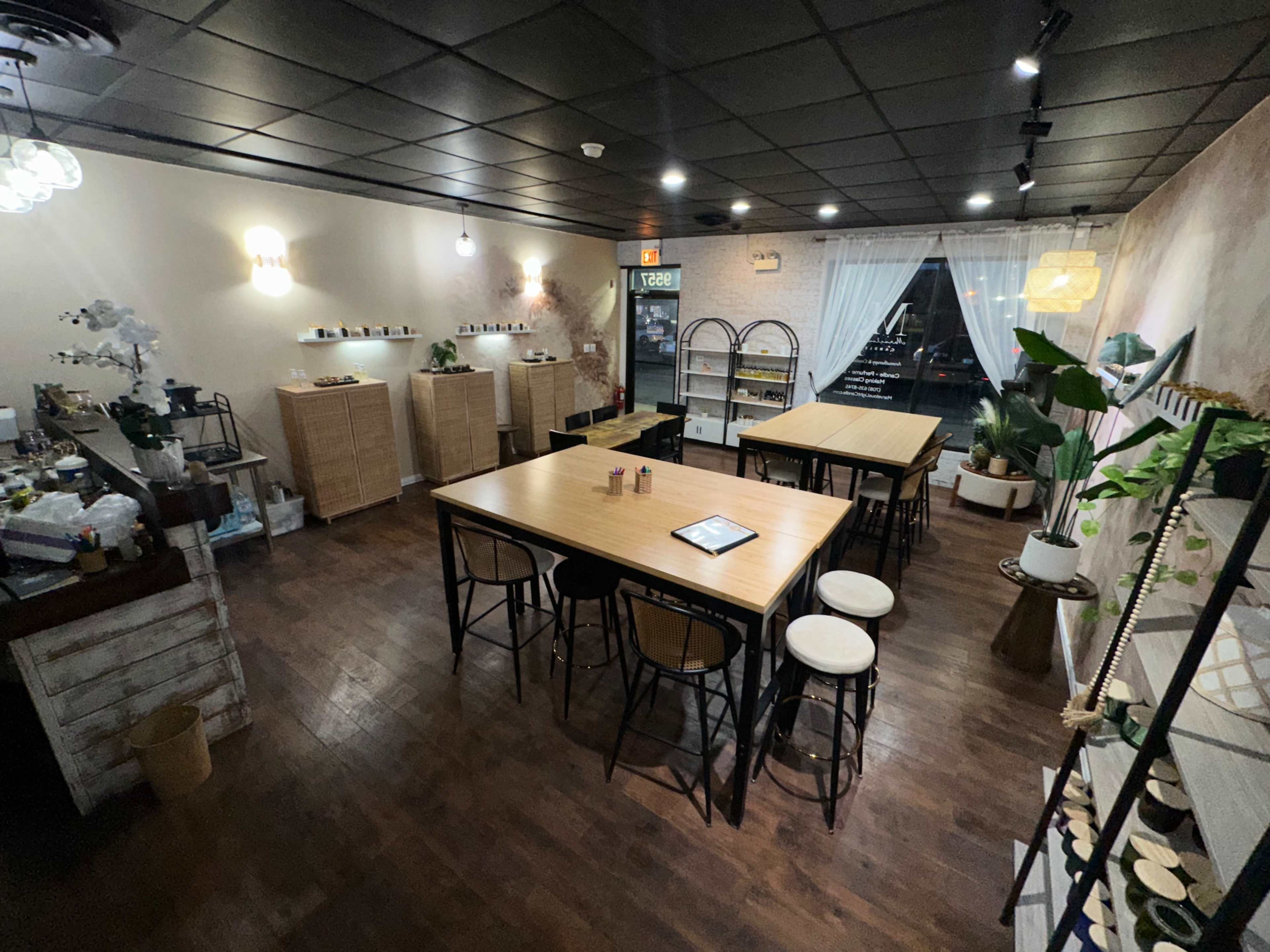 The image shows a cozy interior of a cafe with wooden tables, chairs, and decorative plants, featuring a warm and inviting atmosphere.
