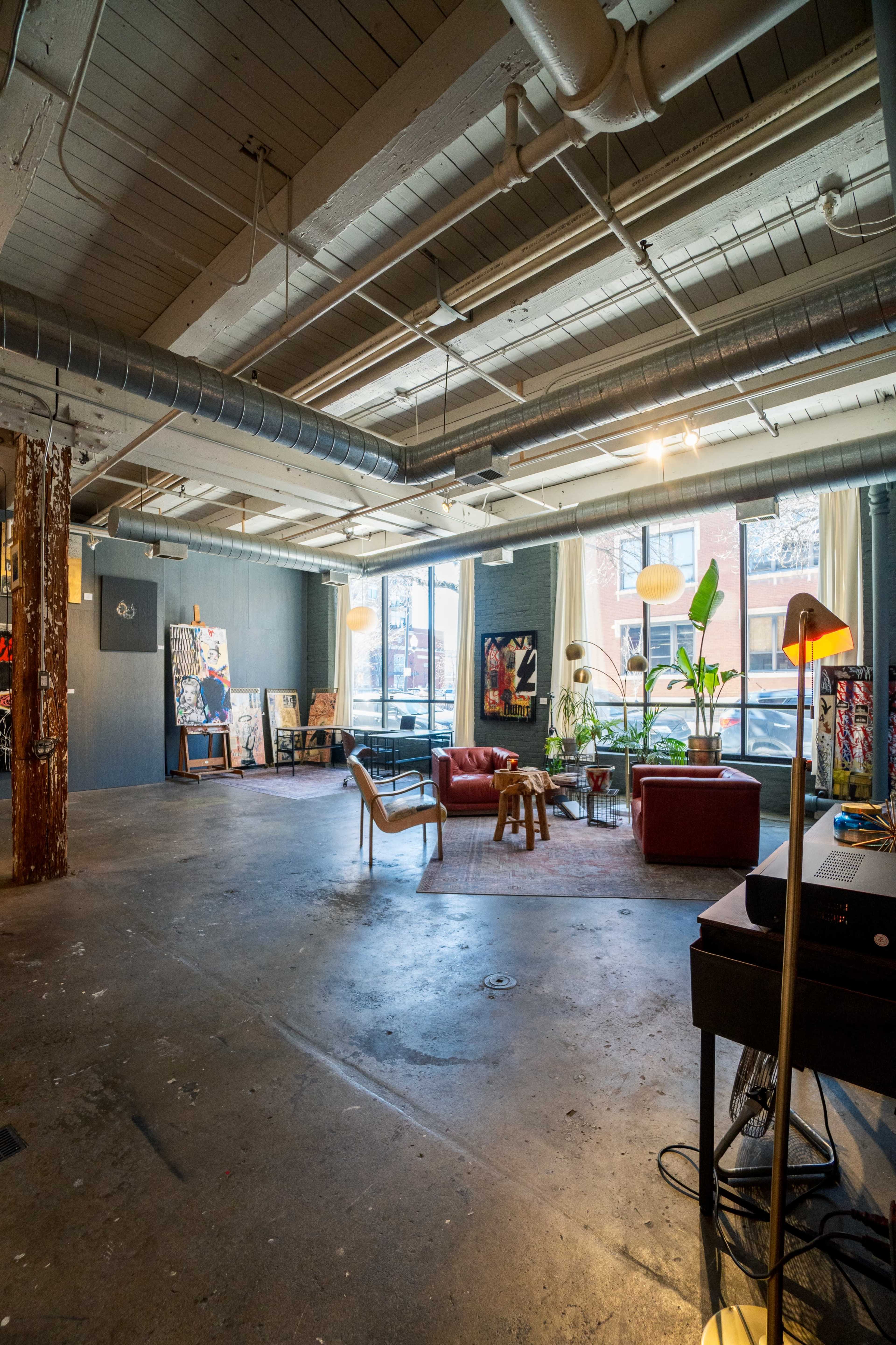 A spacious art studio featuring a red couch, various artworks on the walls, and natural light streaming through large windows.