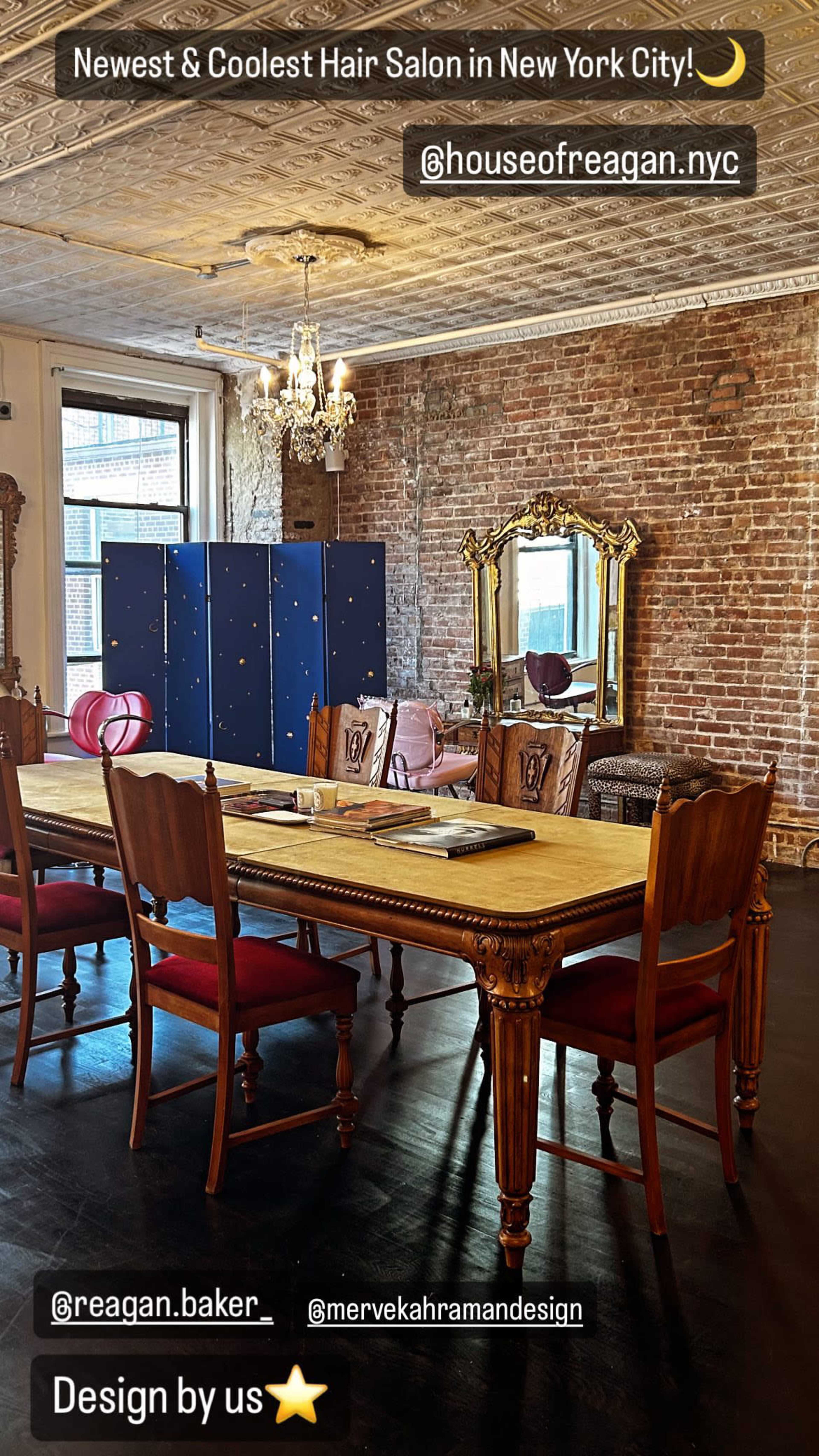 A spacious and stylish hair salon features a long wooden table surrounded by elegant chairs, set against a backdrop of exposed brick walls.