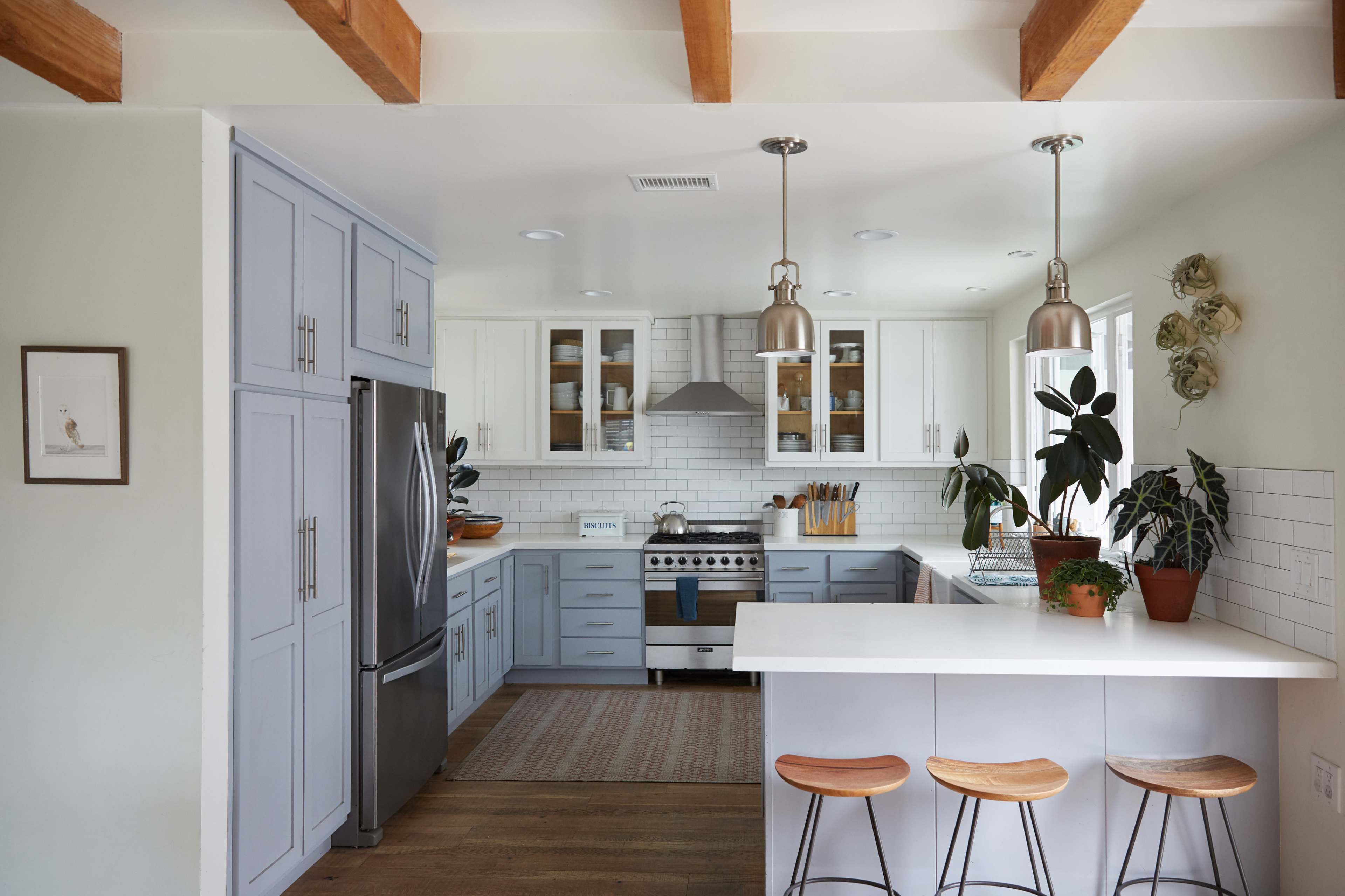 The image shows a modern kitchen featuring light blue cabinetry, stainless steel appliances, and a white countertop with bar stools.