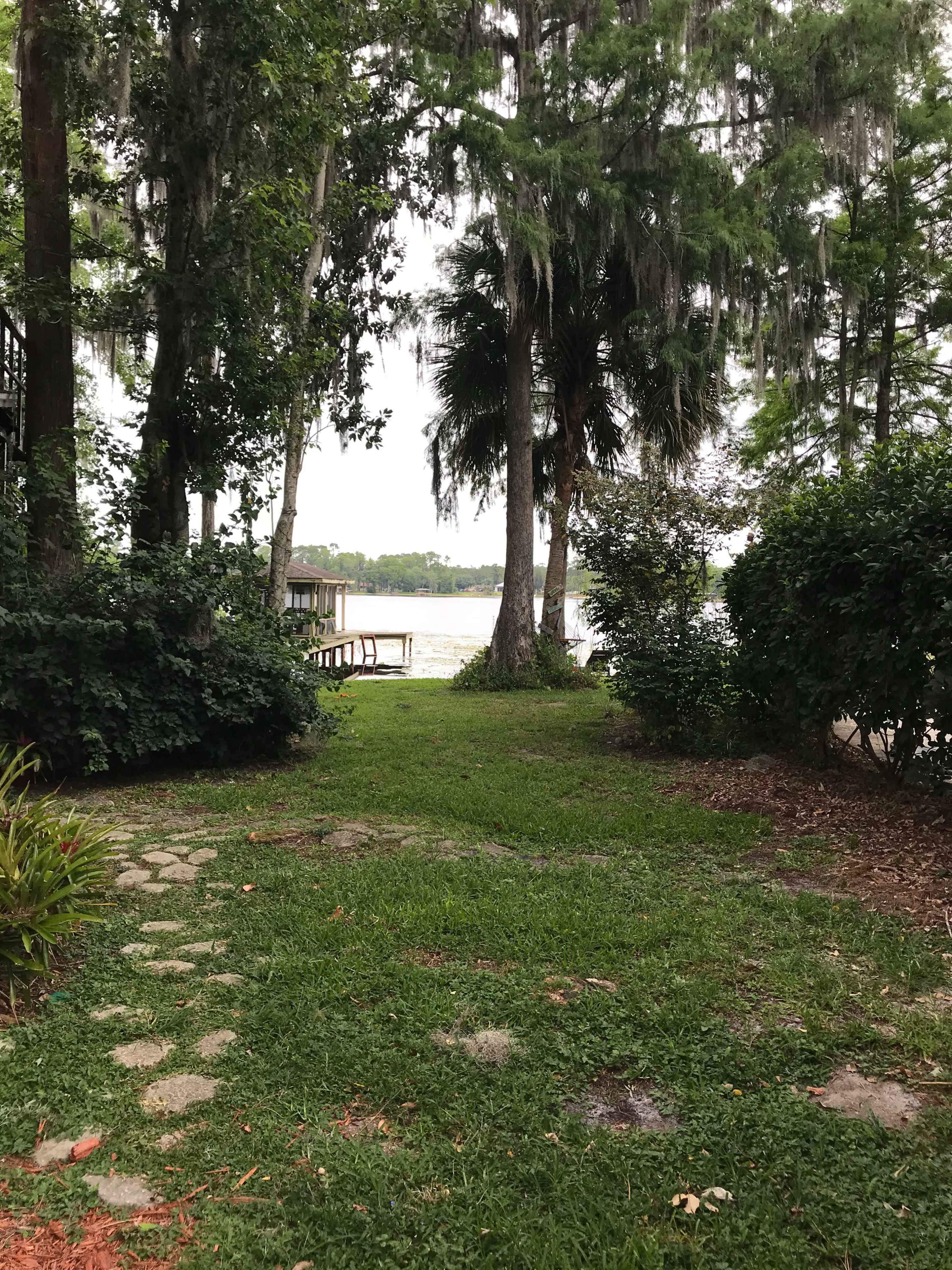 A path of stones leads through greenery to a lake surrounded by trees.
