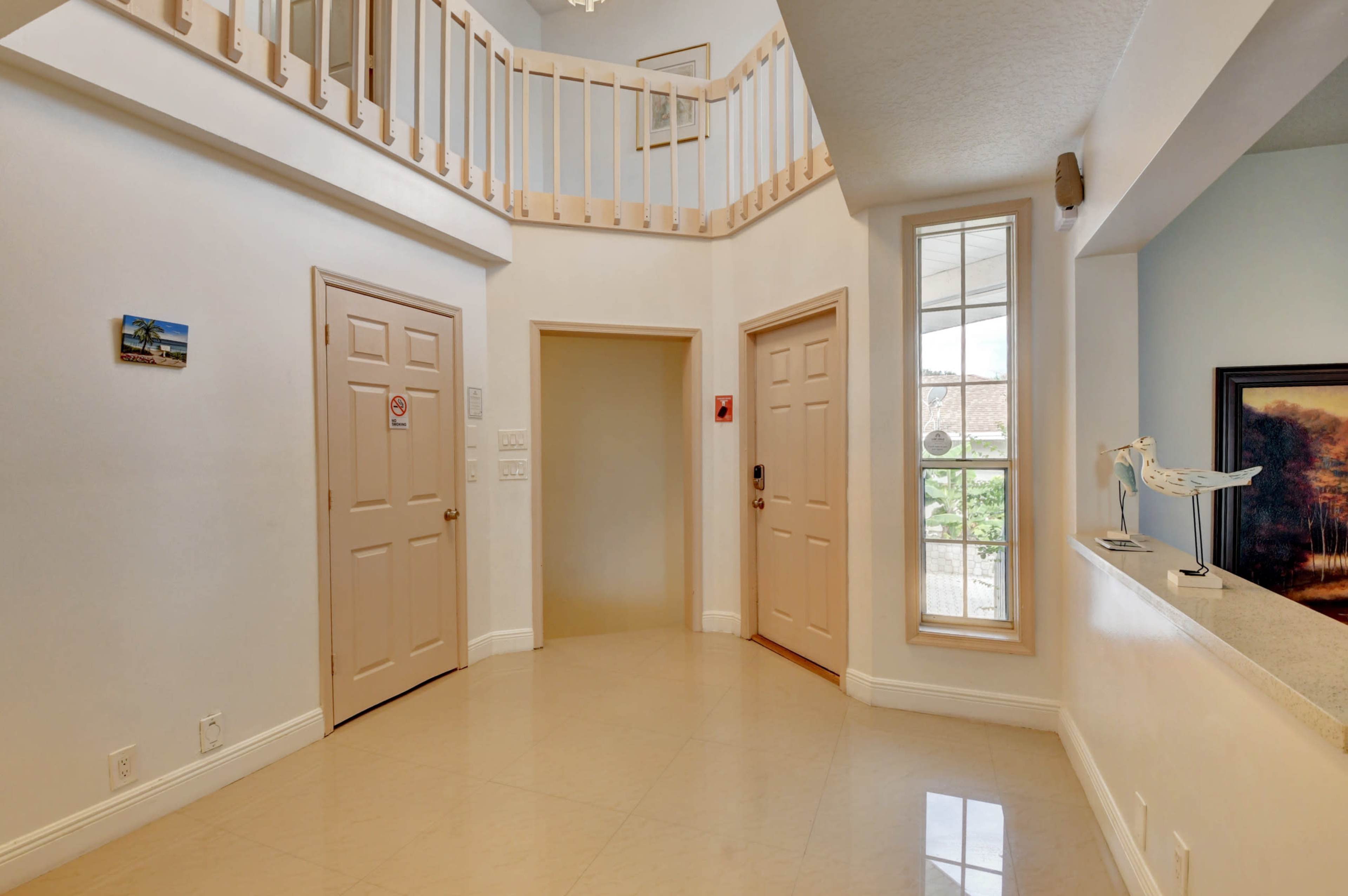 The image shows a light-colored foyer with tan doors on either side and a staircase leading to a balcony above.