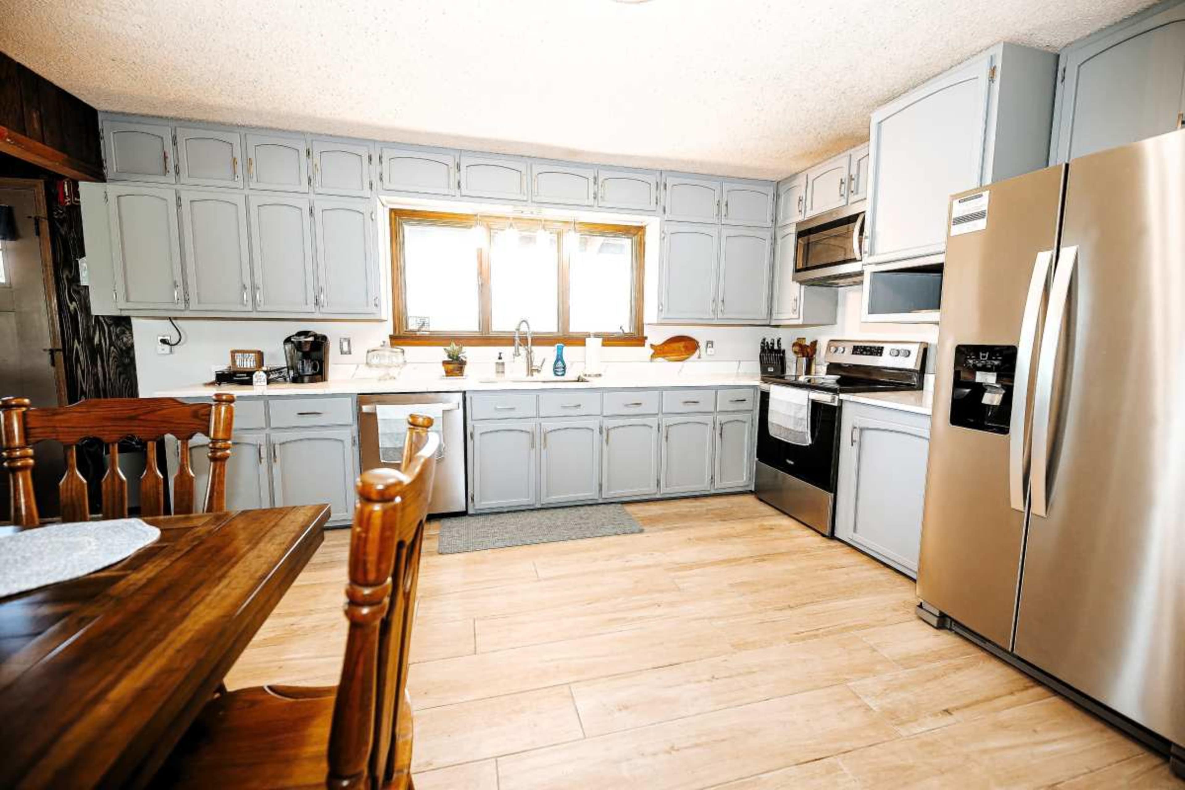 The kitchen features light gray cabinetry, stainless steel appliances, and a wooden dining table.