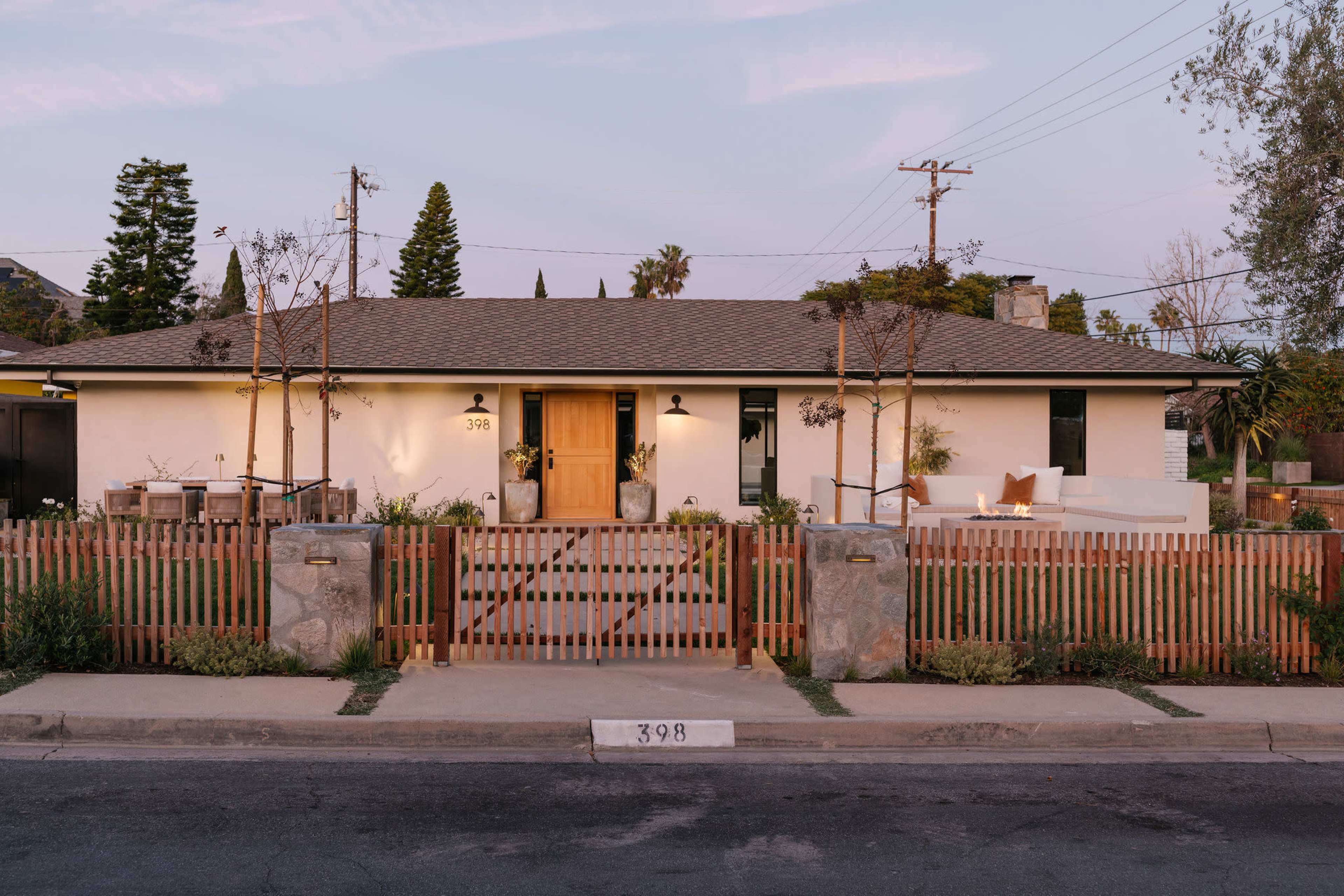 The image shows a single-story house with a light exterior, modern landscaping, and a wooden fence surrounding the front yard.