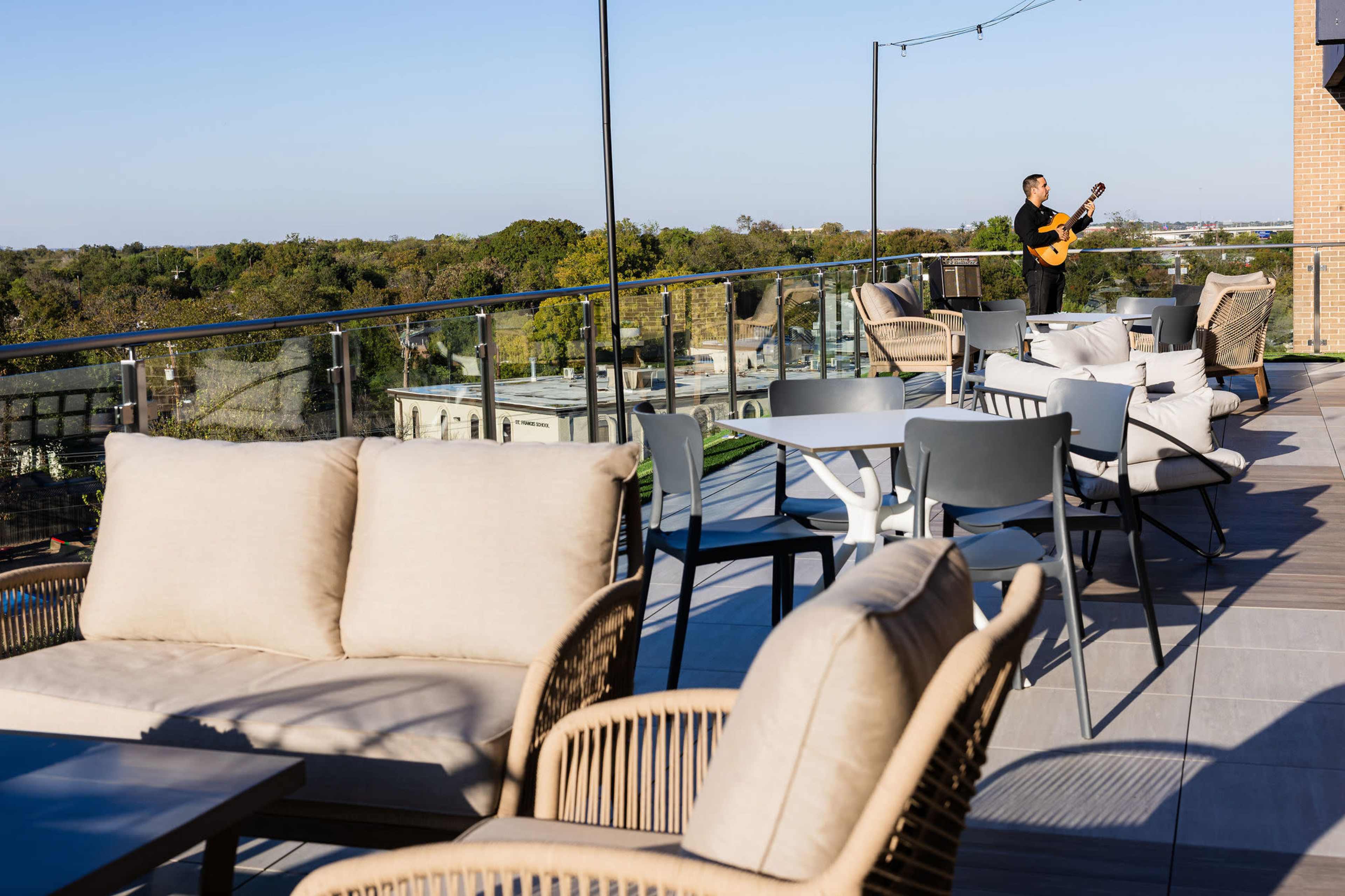 A musician plays guitar on a rooftop terrace adorned with modern furniture and a view of the surrounding landscape.