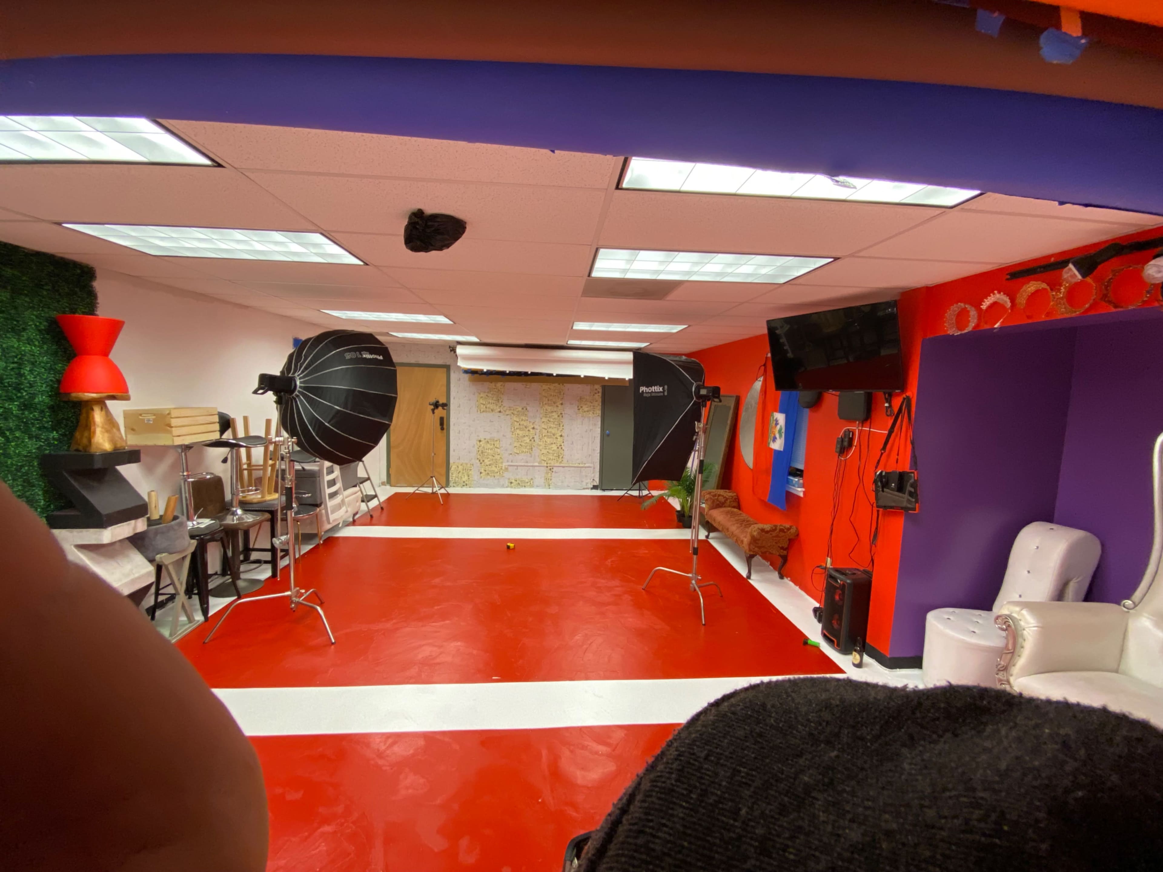 A spacious studio setup with red flooring, two large lighting tents, and various backdrops arranged along the walls.