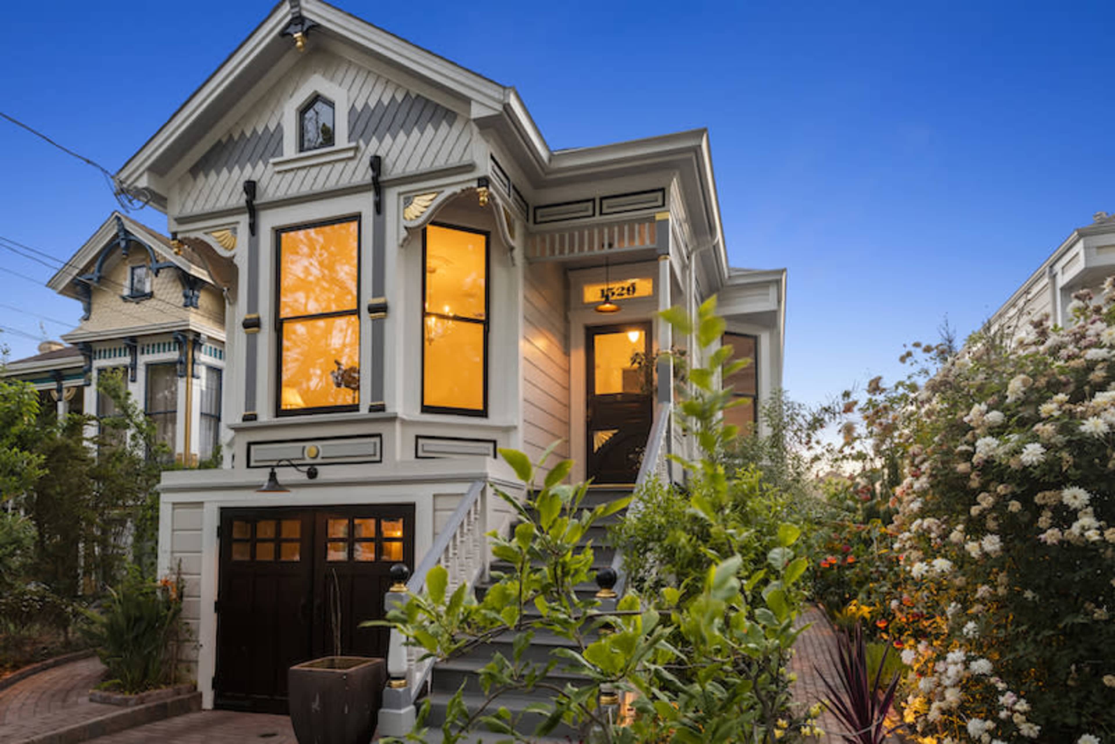 A Victorian-style house with large windows and a landscaped front garden is illuminated by evening light.