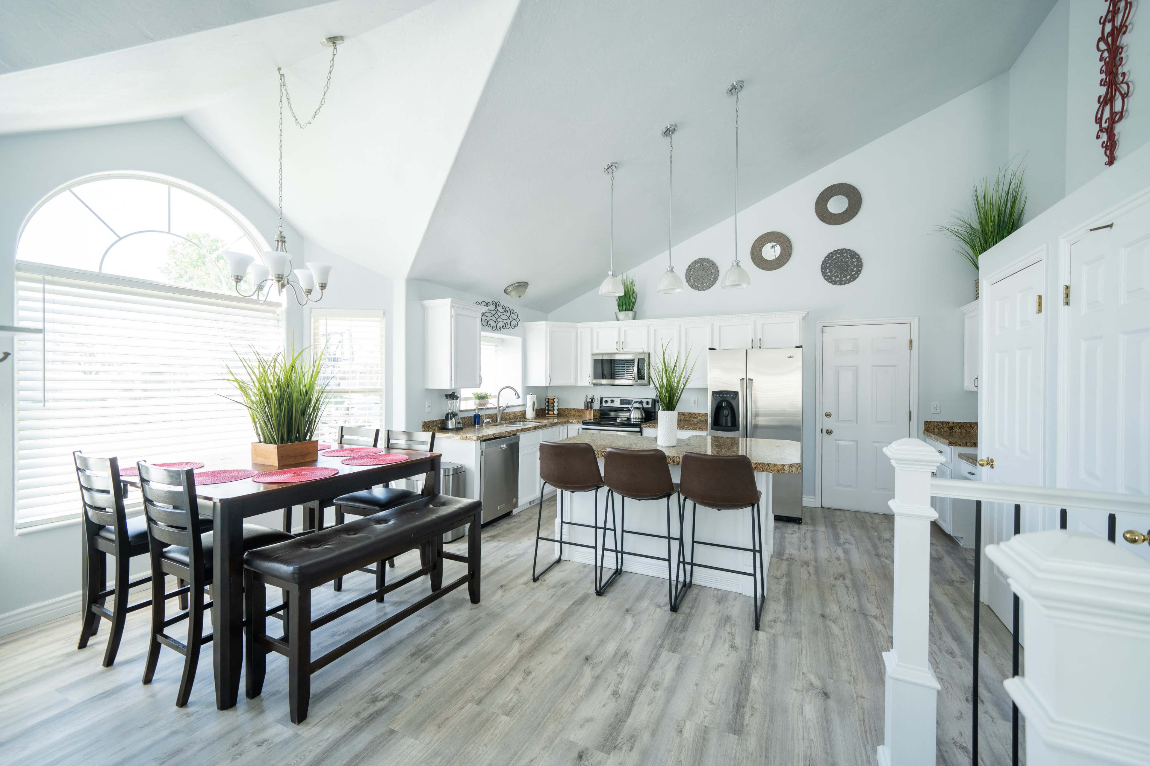 A modern kitchen with white cabinetry, a large dining table, and a bar area featuring three brown stools.