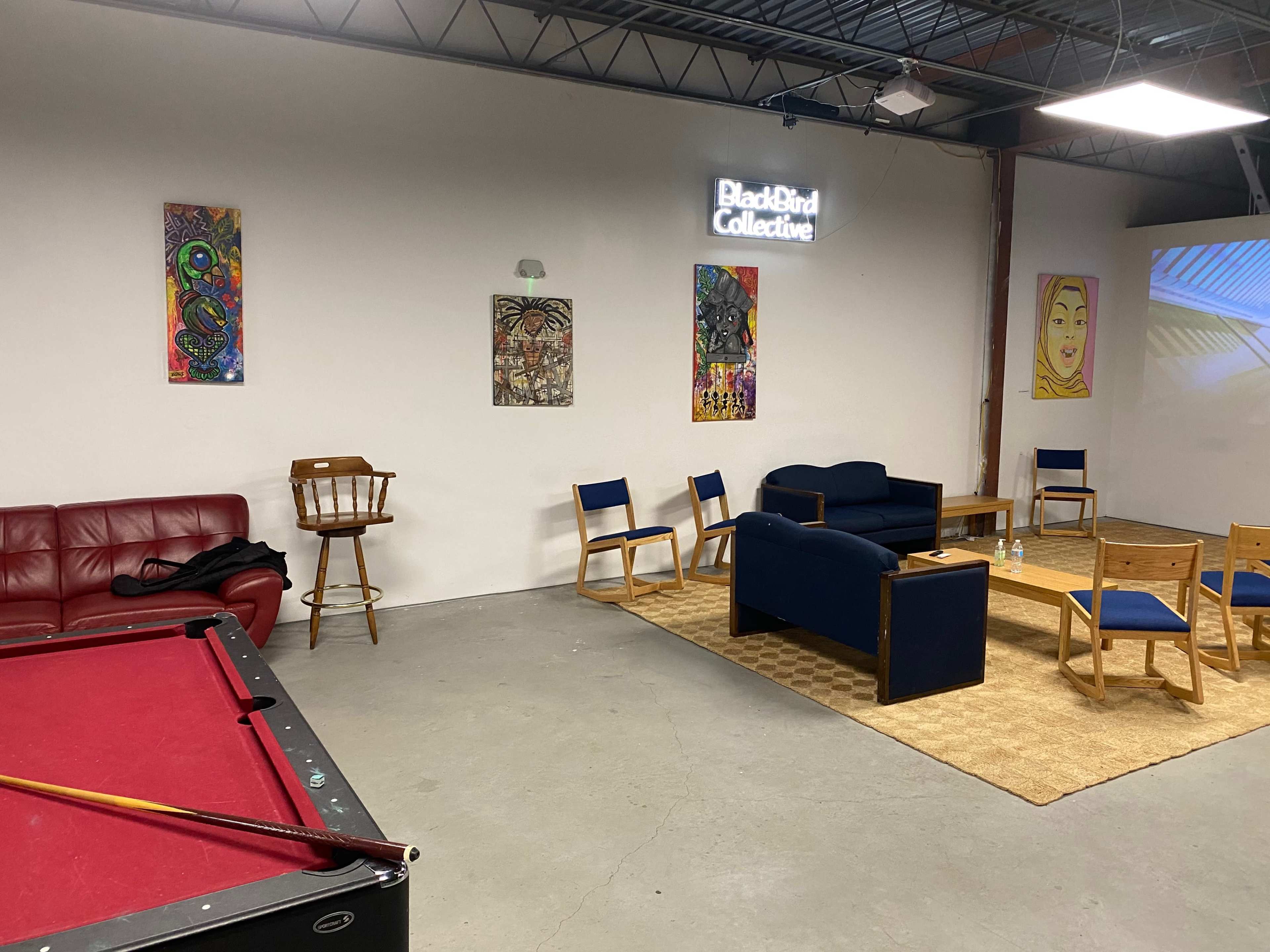 A spacious lounge area with a red pool table, a seating arrangement of blue and wooden chairs, and artwork displayed on the walls.