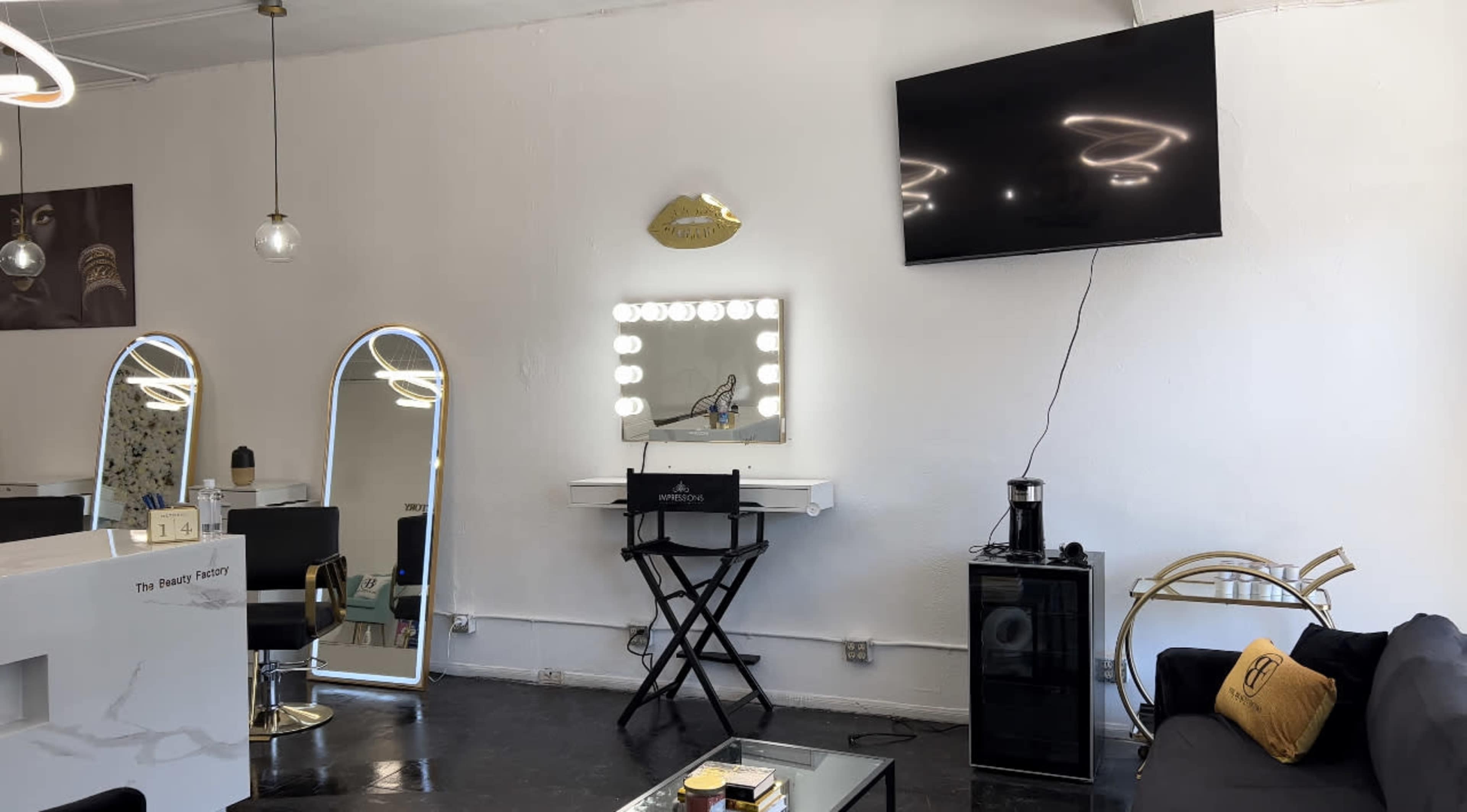 A modern salon interior featuring three mirrors, a large television mounted on the wall, and a seating area with a coffee table.