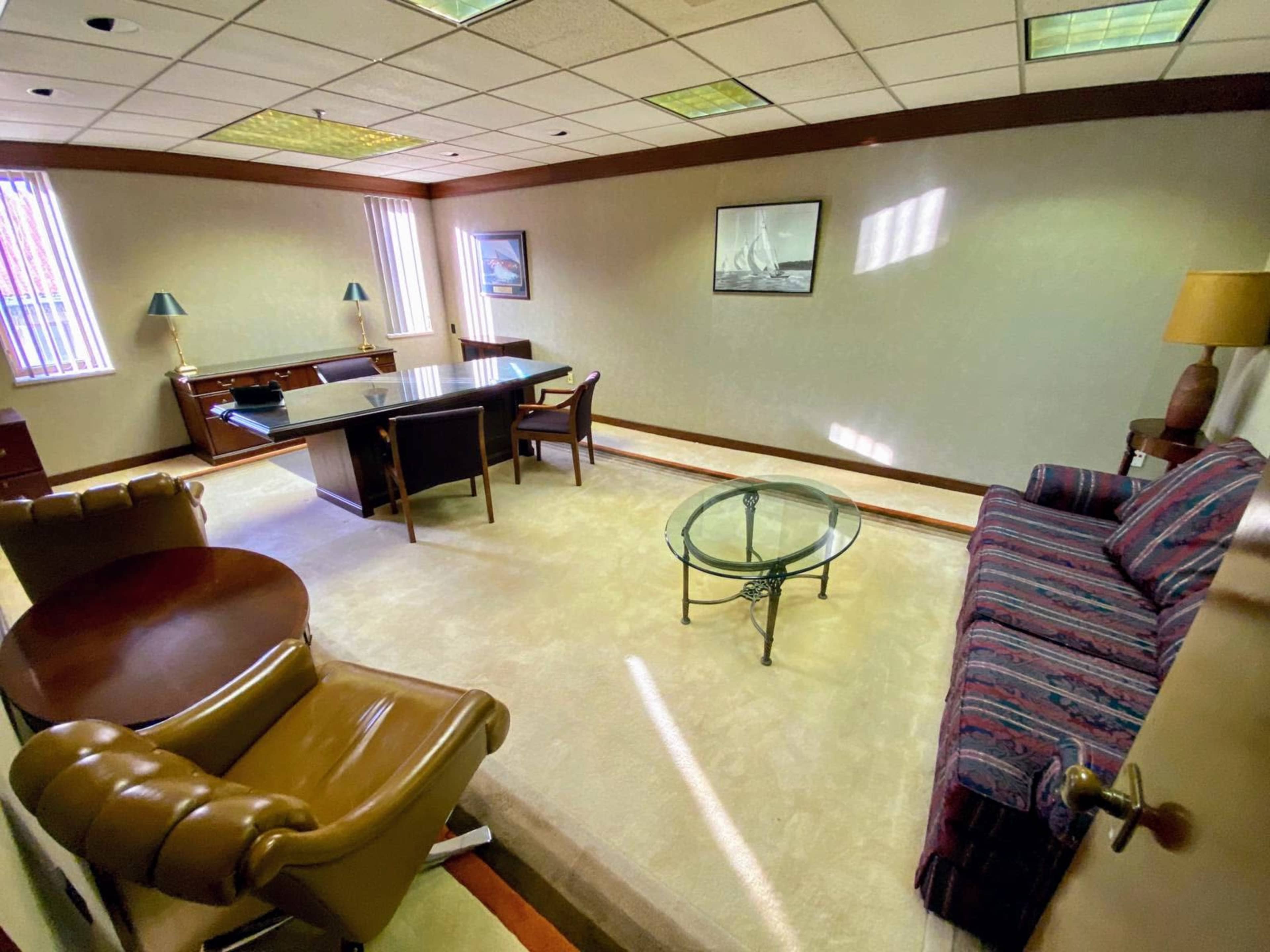 The image shows a well-furnished office featuring a desk, chairs, a coffee table, and decorative wall art.