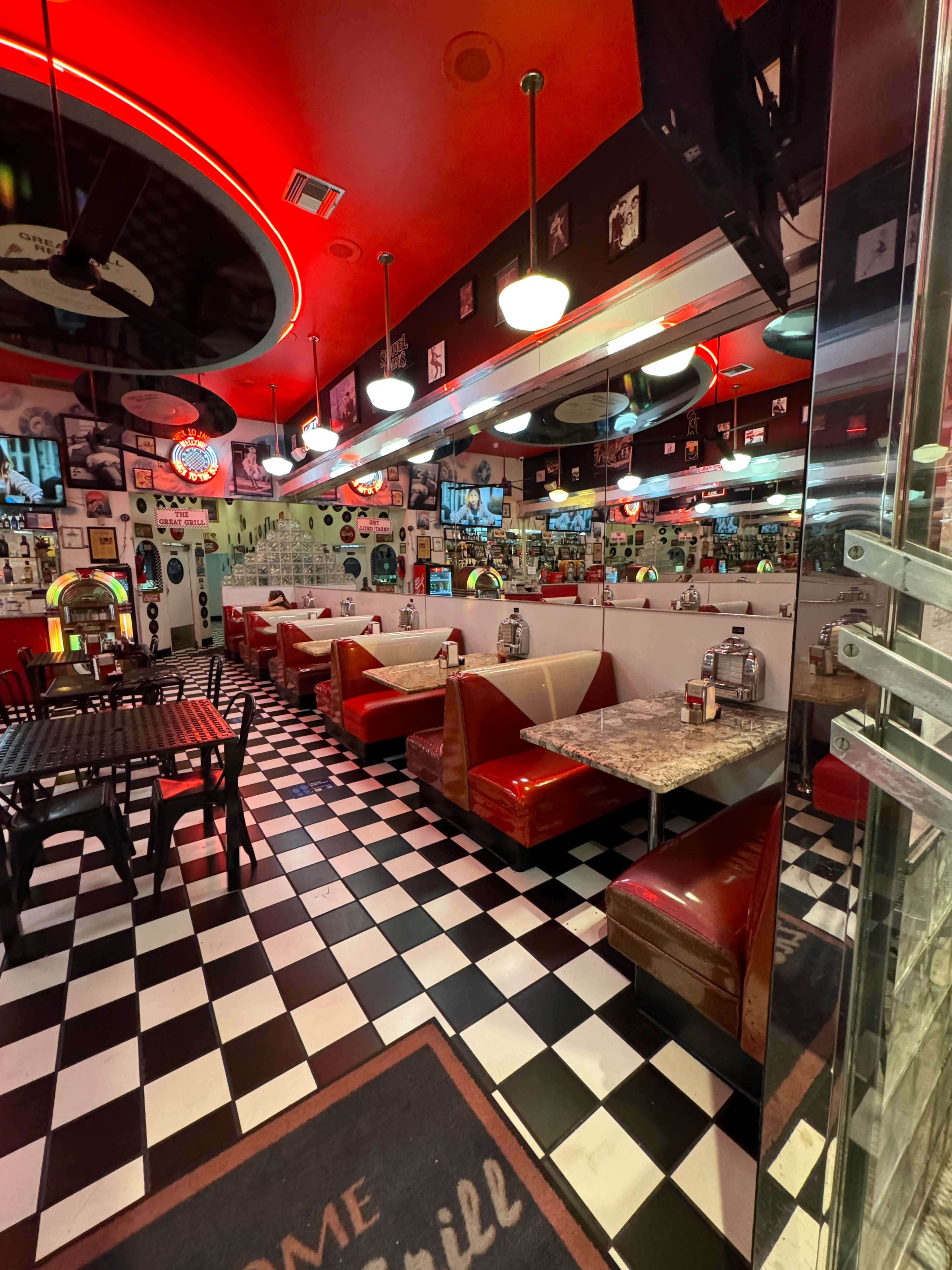 The image shows a retro diner interior with red and white booths, black and white checkered flooring, and various wall decorations.
