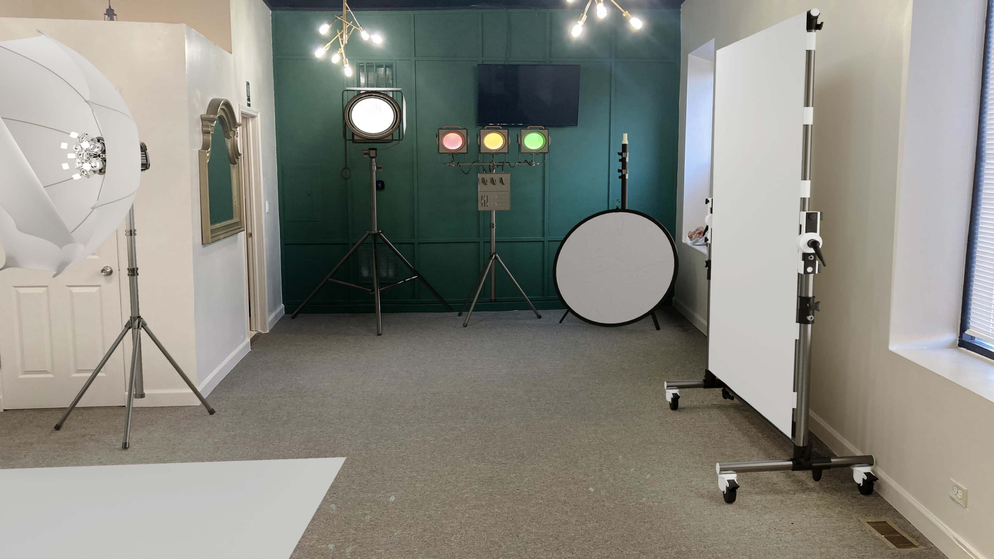 A well-lit studio space featuring various photography equipment, including a large softbox, a spotlight on a stand, and a reflector, all arranged against a green wall.