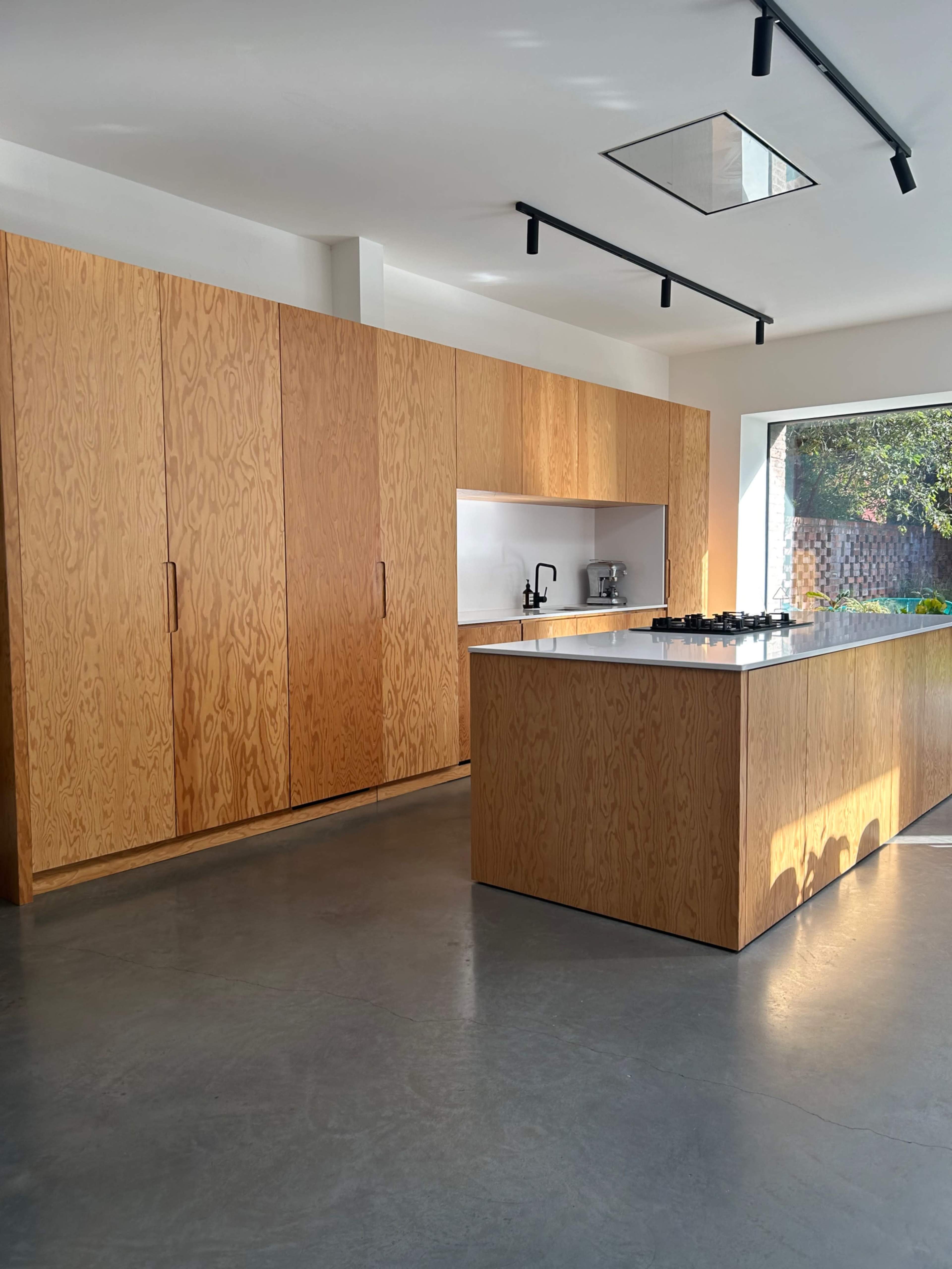 The kitchen features light wood cabinetry, a central island with a gas cooktop, and a large window providing natural light.