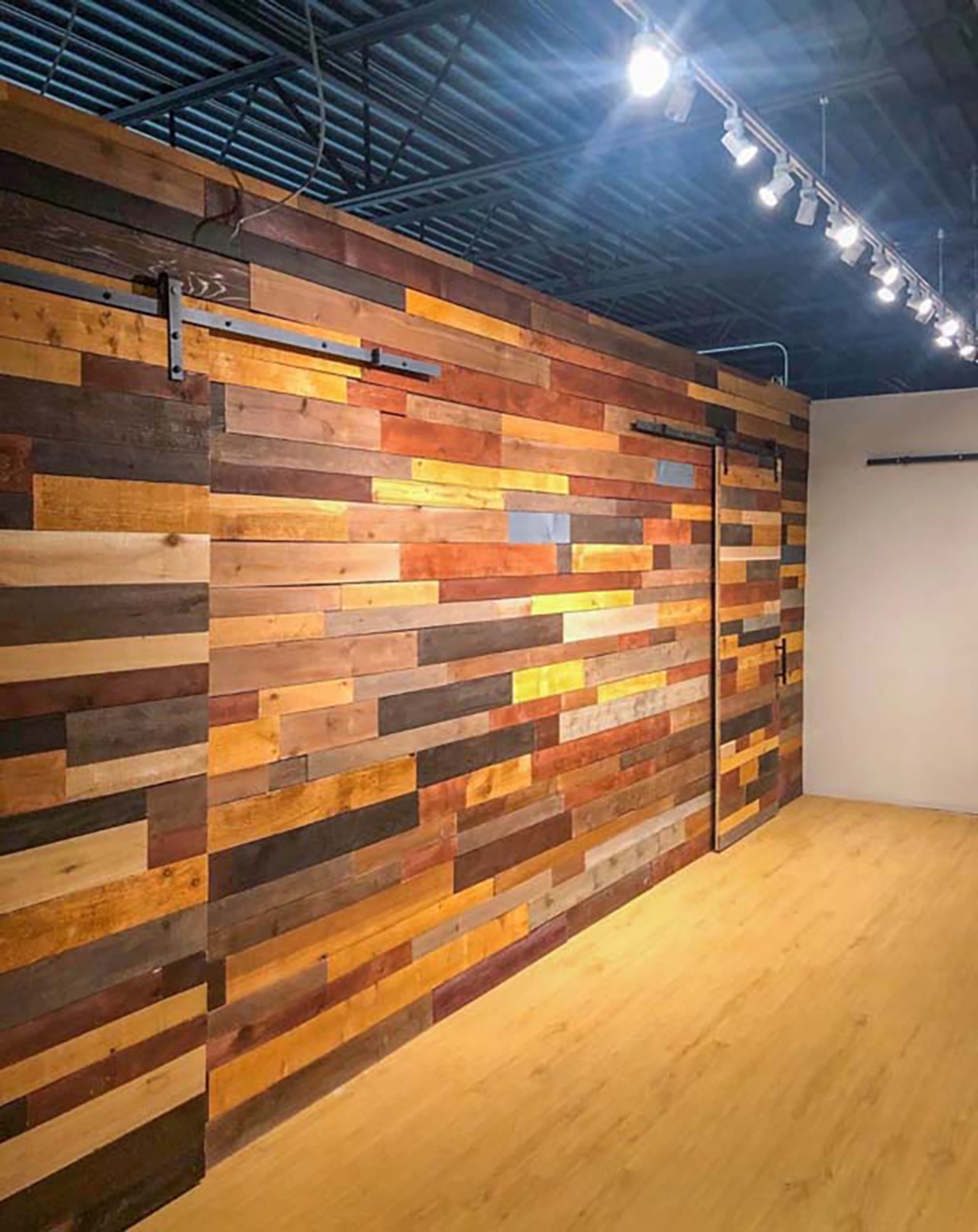 A wall made of various wood planks in different shades arranged horizontally, with a light fixture above illuminating the space.
