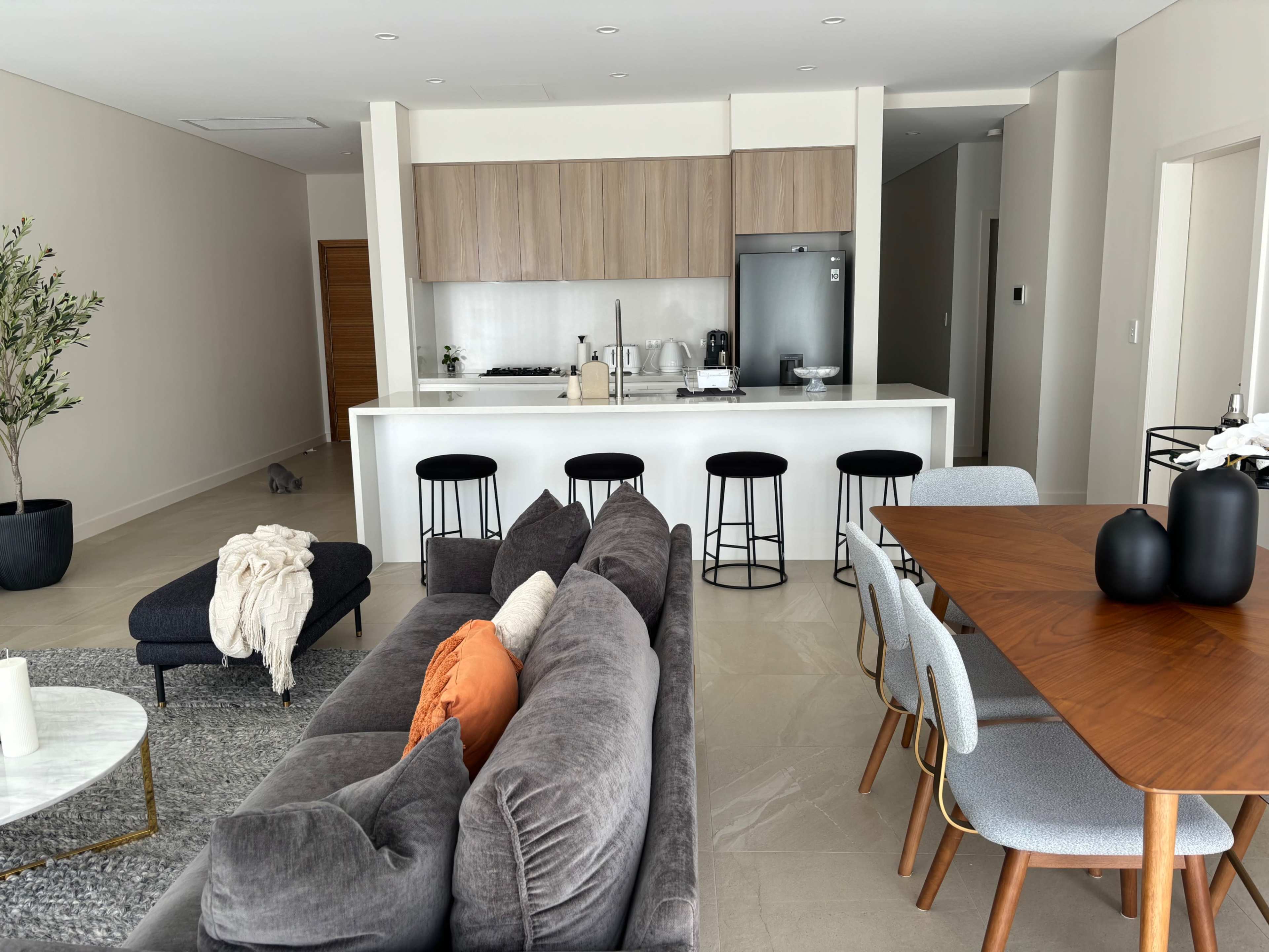 A modern open-concept living area with a sofa, dining table, and a kitchen in a bright, minimalist design.