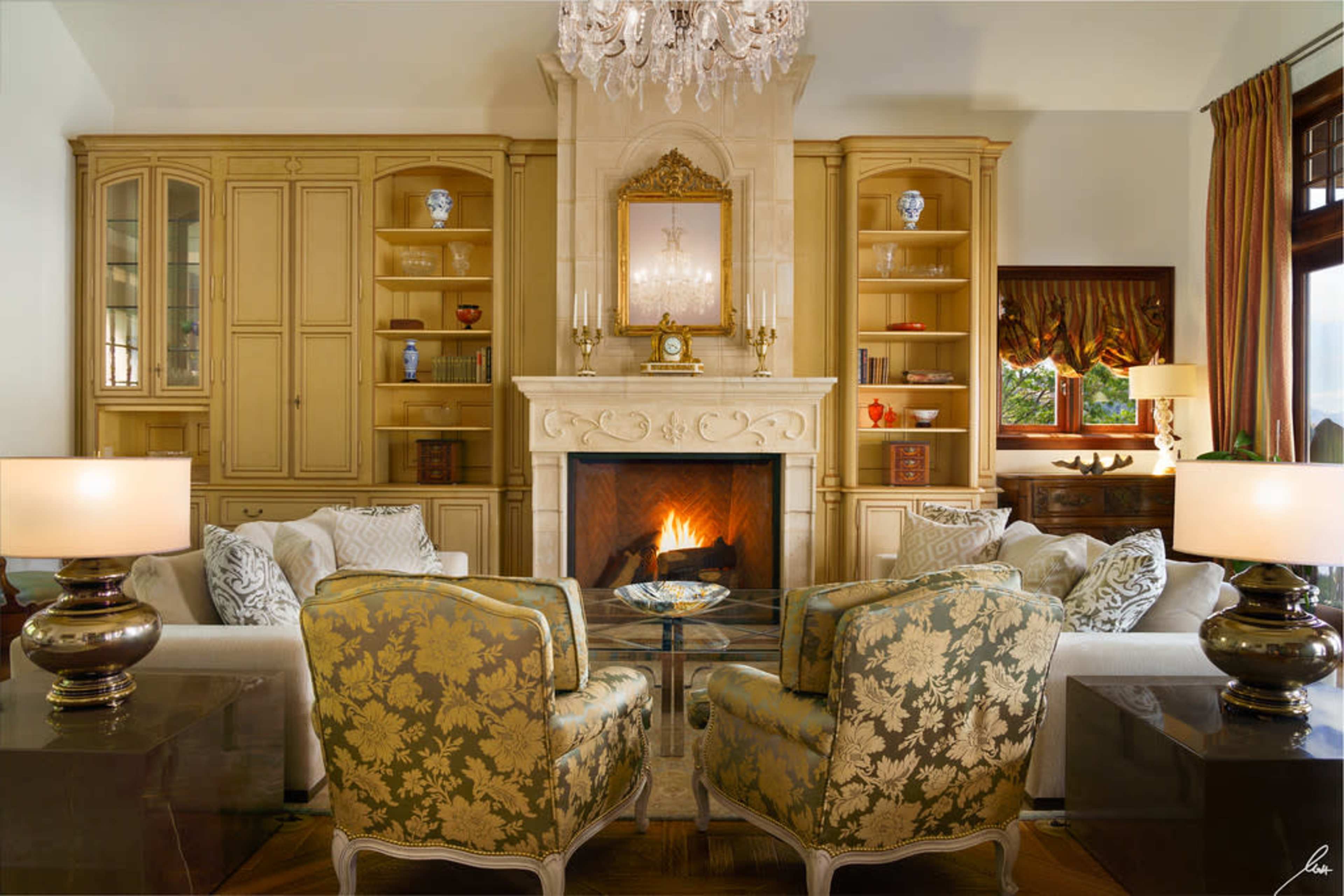 A elegantly furnished living room with a central fireplace, two patterned armchairs, and built-in shelves displaying decorative items.