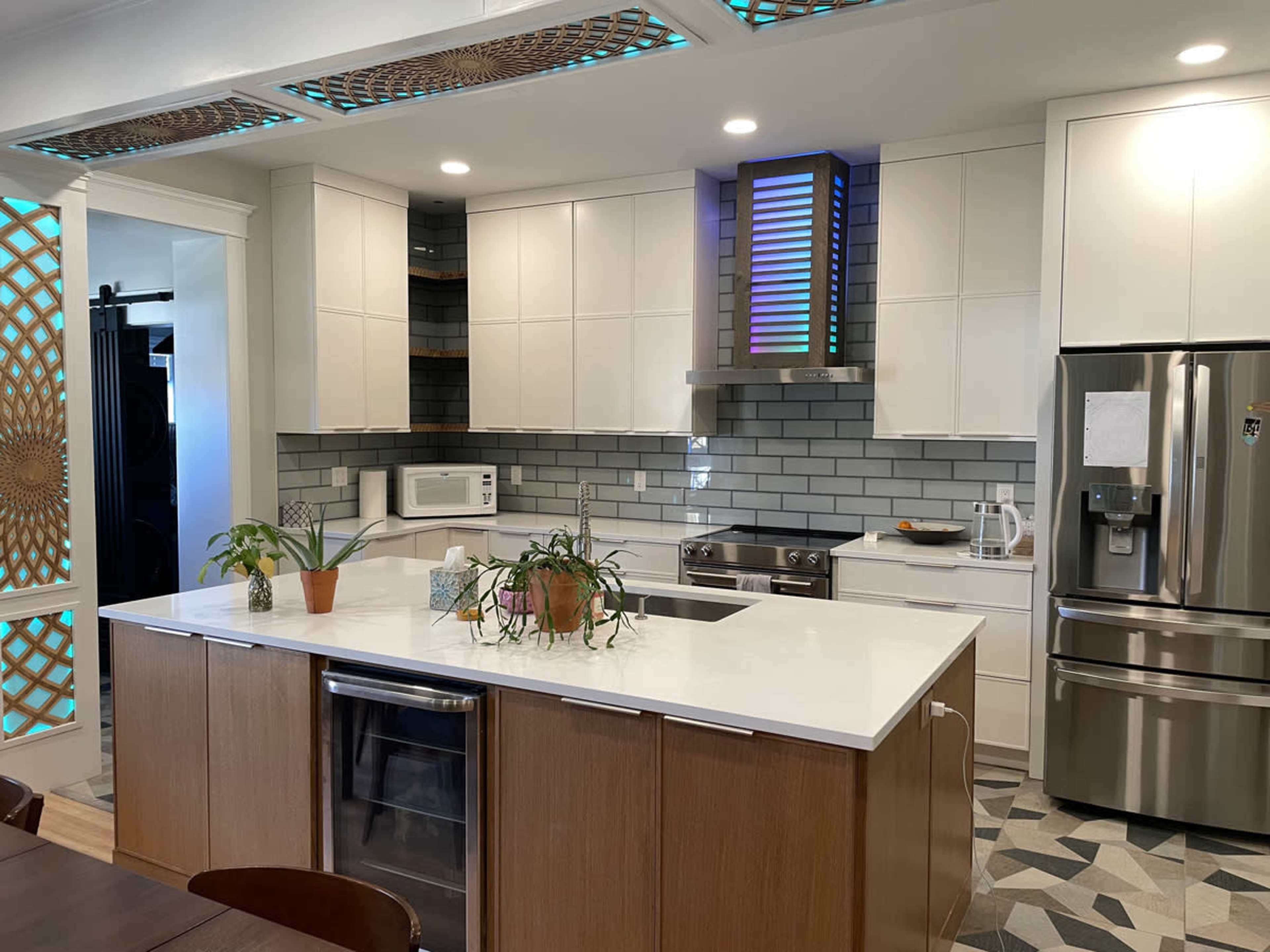A modern kitchen features white cabinets, a large island with a sink, stainless steel appliances, and a patterned tiled floor.