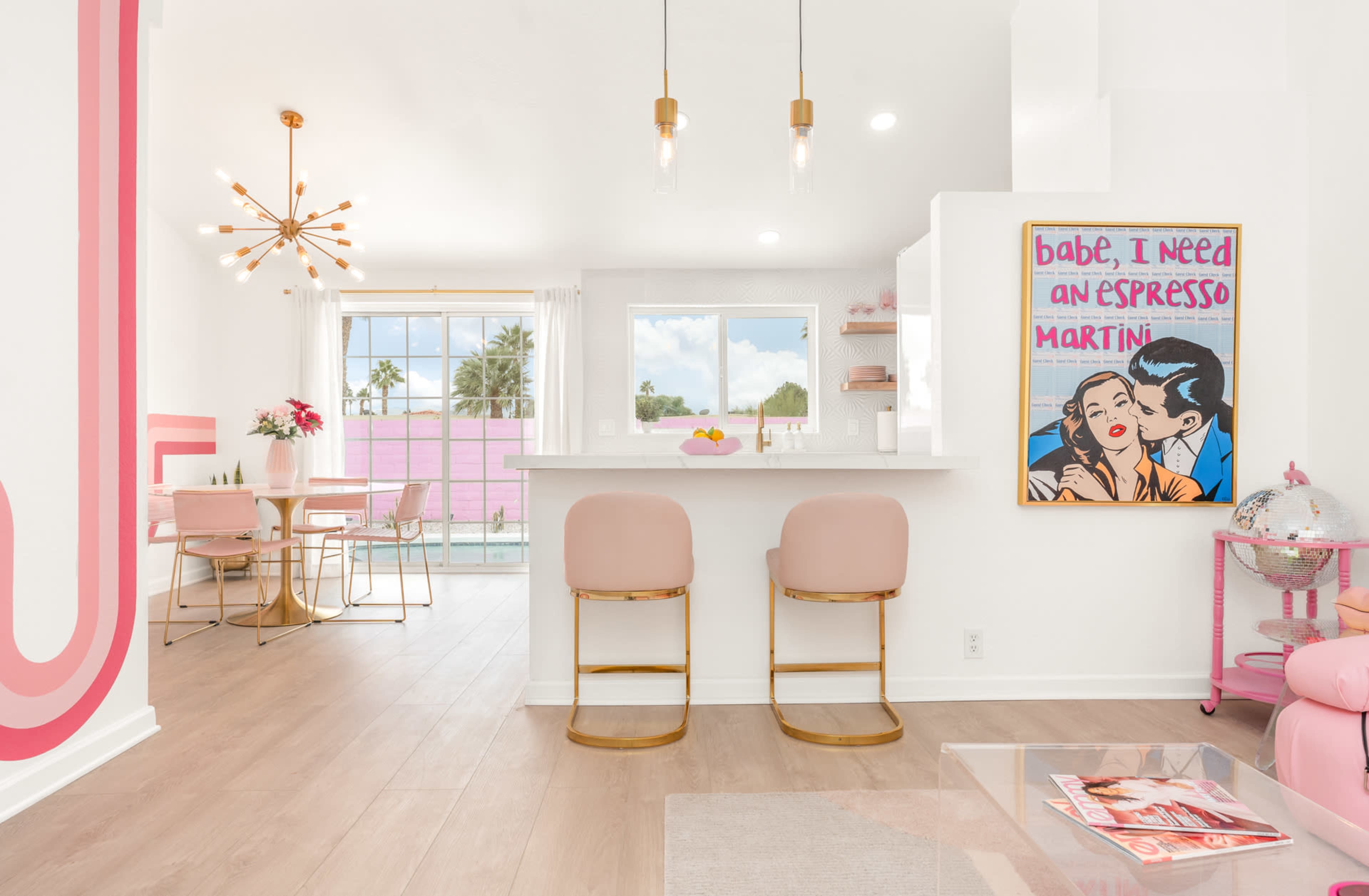 A bright, modern interior featuring a kitchen with bar stools, a dining area, and a colorful artwork on the wall.