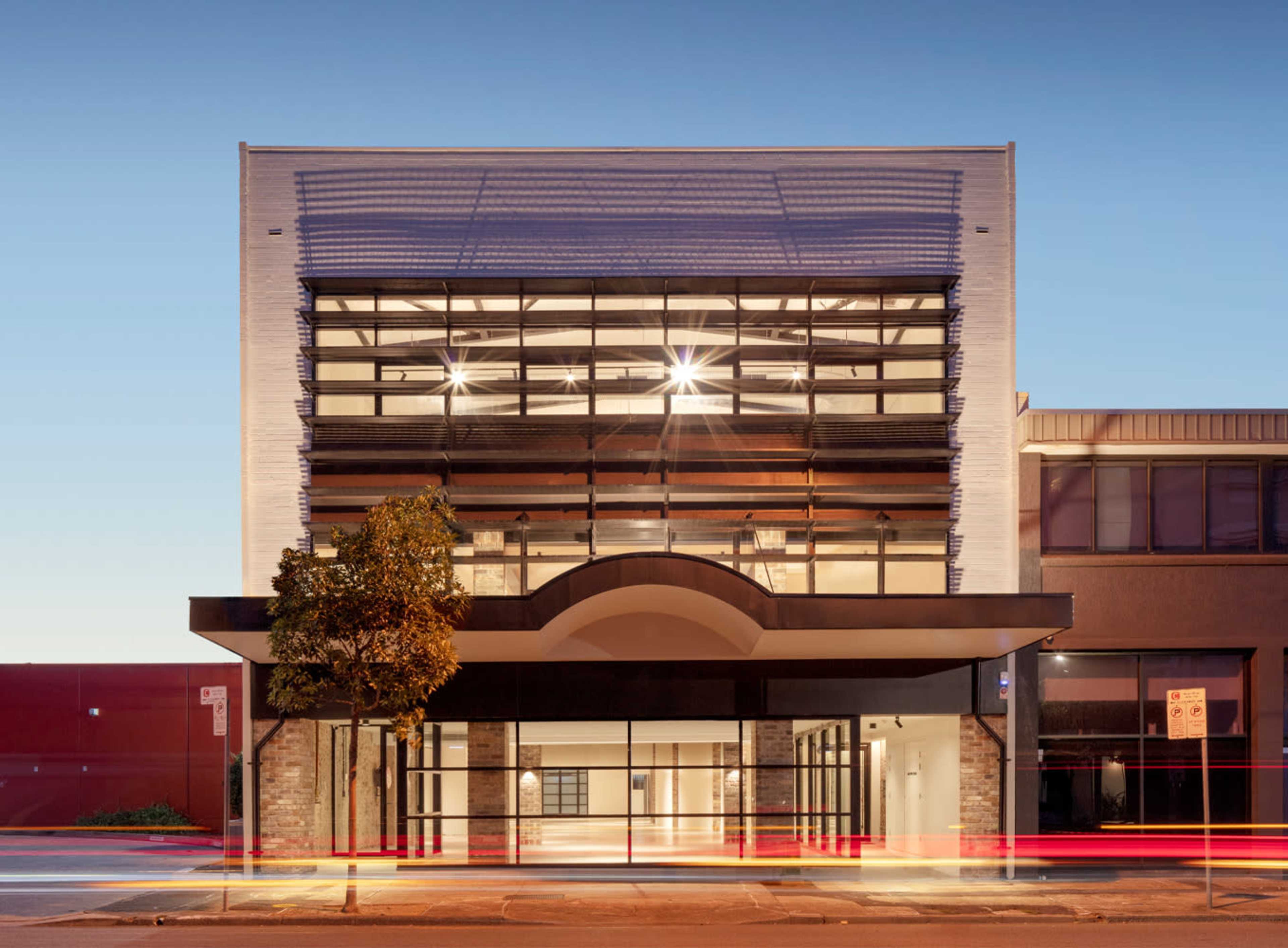 A modern building with large glass windows and a distinctive arch over the entrance, illuminated by interior lighting.