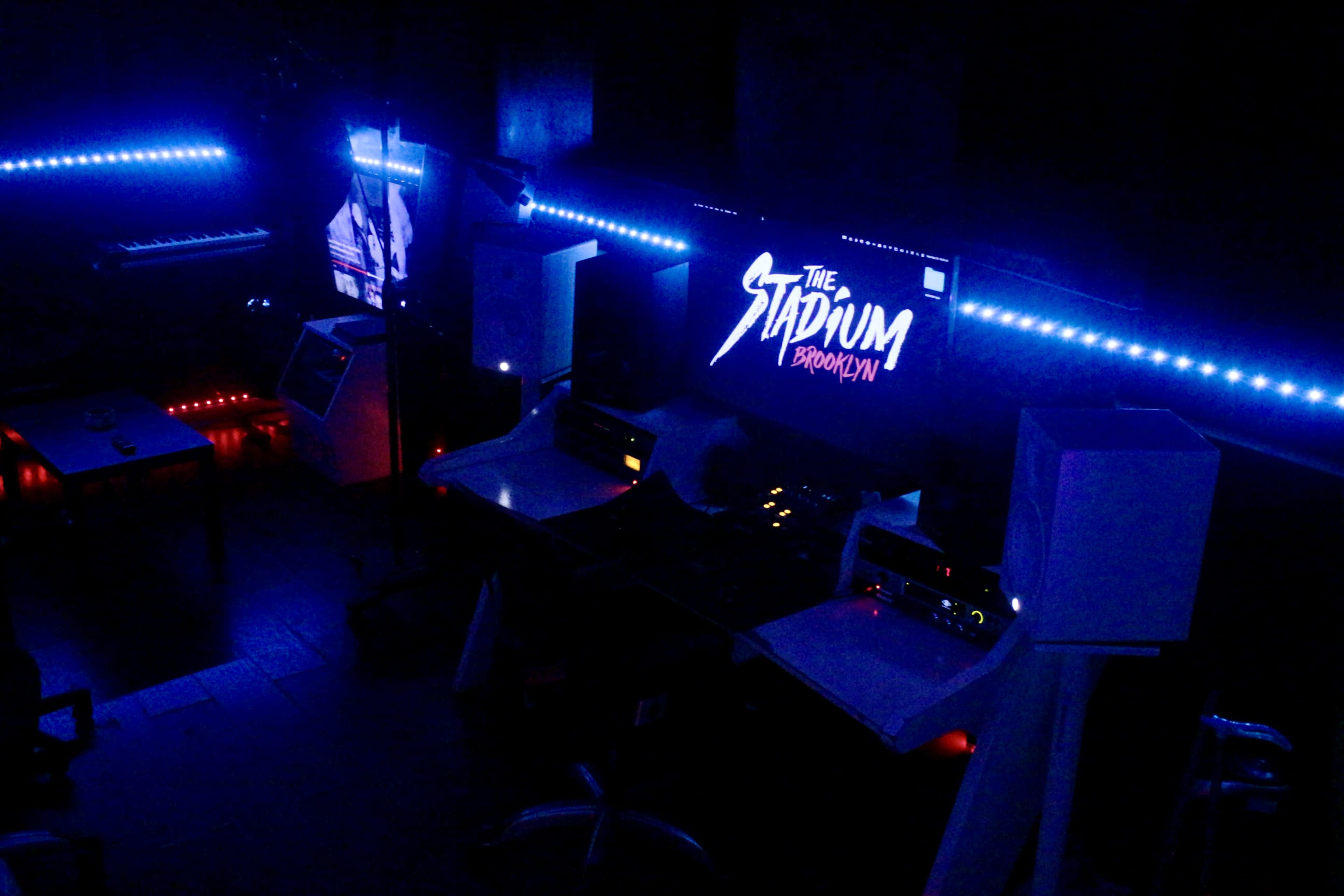 The image shows a dimly lit room featuring multiple sound production stations and illuminated LED strips along the walls.