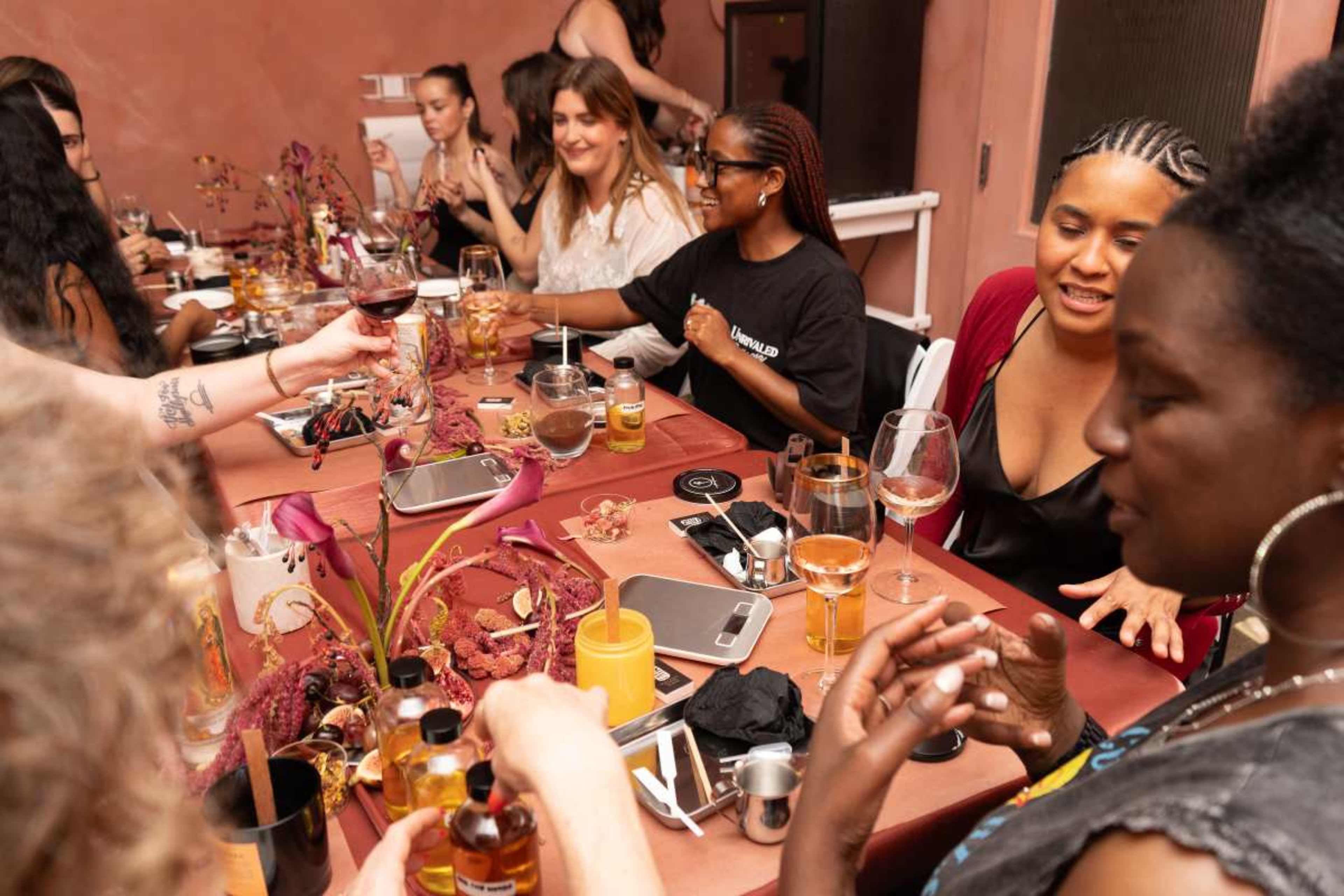 A group of women are seated around a table adorned with floral decorations and food, engaging in conversation while enjoying drinks.