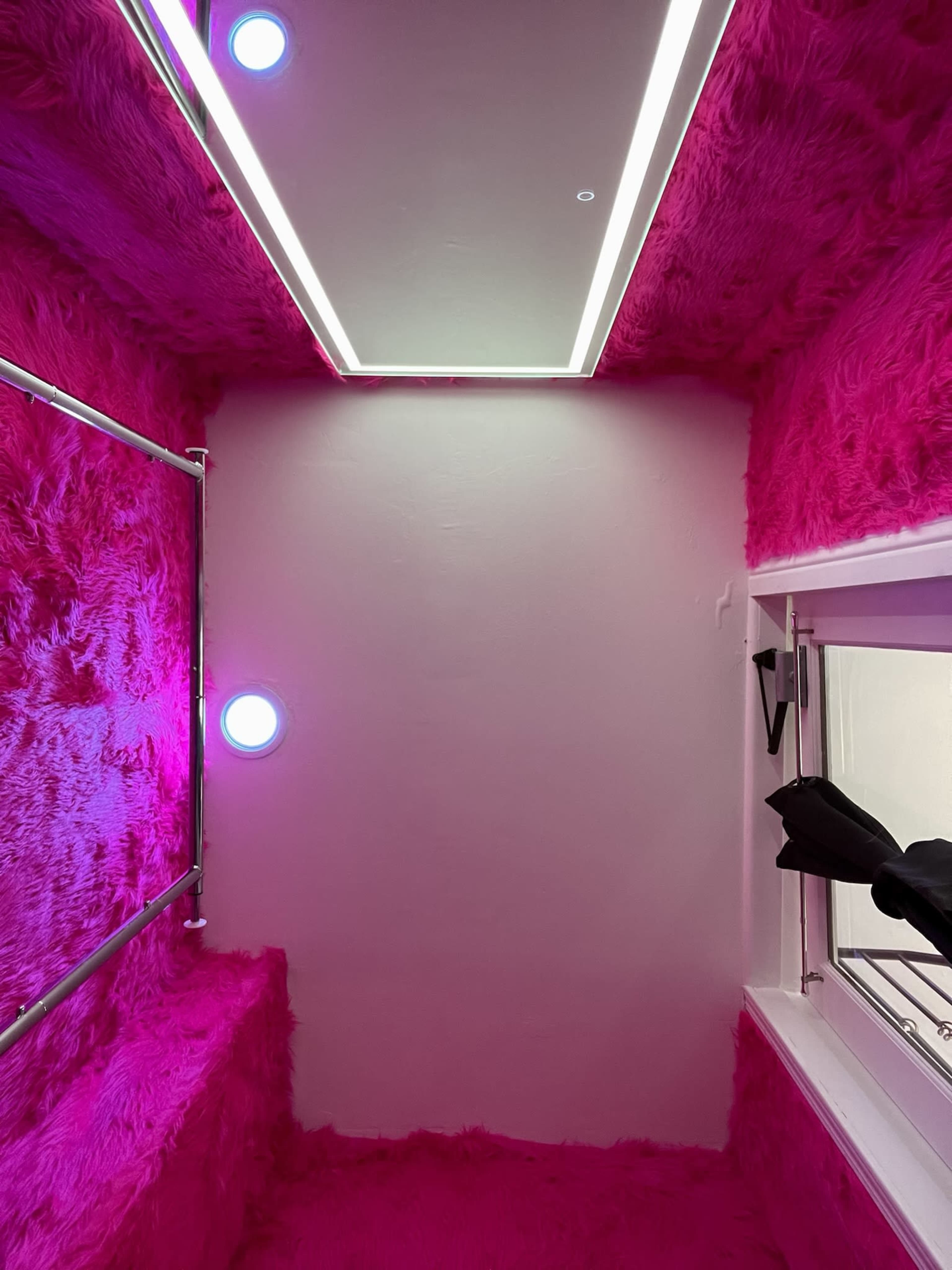 A small room with plush pink walls, a mirror on the ceiling, and circular lights on the walls.