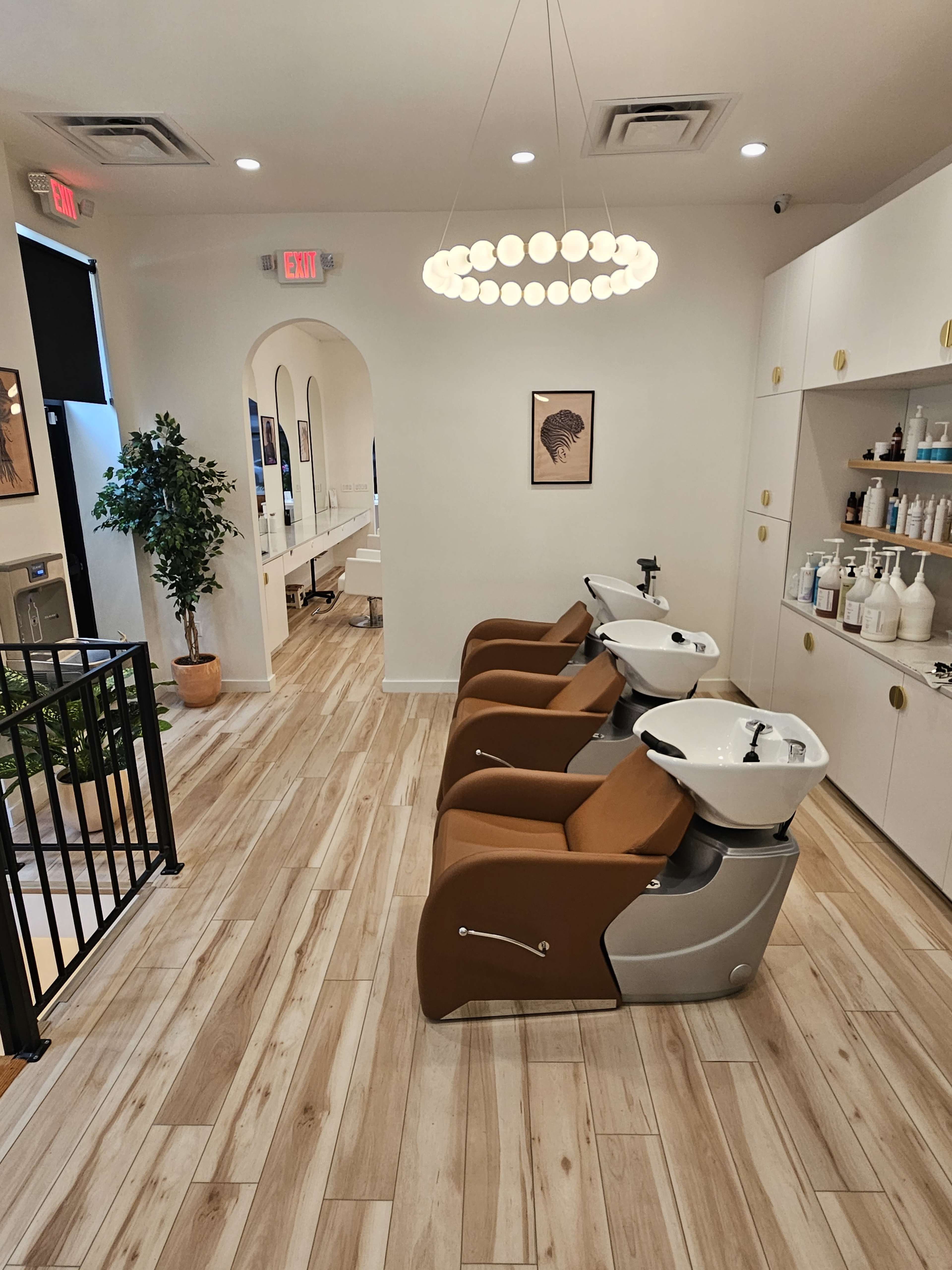 A modern salon interior with three shampoo stations, light wood flooring, and a round pendant light.
