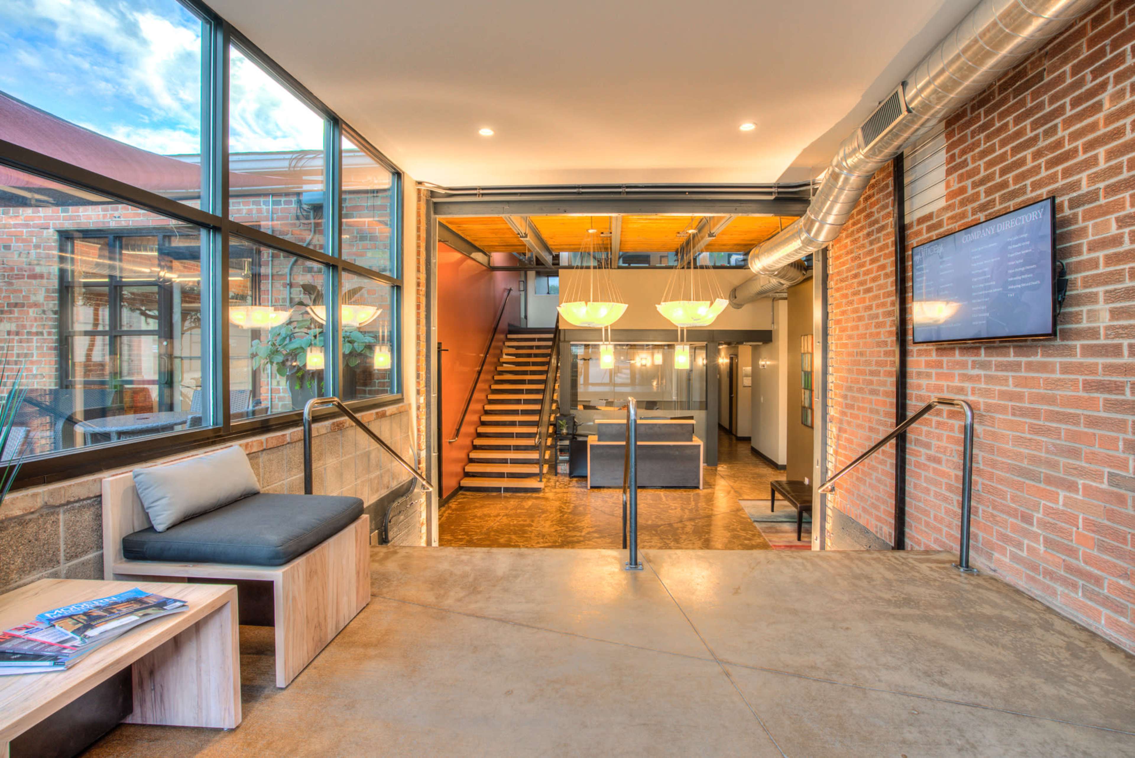 A modern interior space featuring an open area with large windows, a staircase leading to an upper level, and a seating area with a wooden bench and a coffee table.