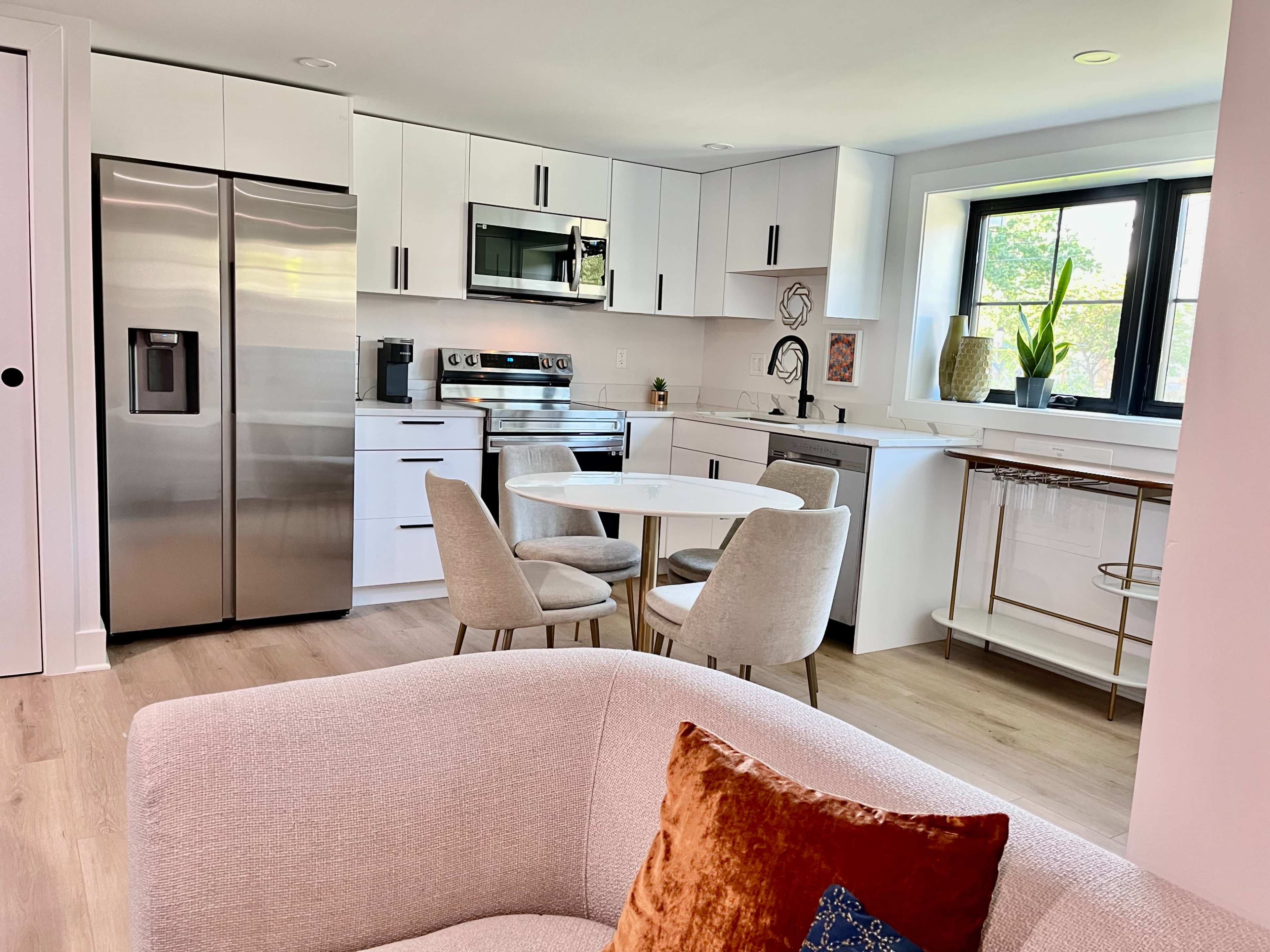 A modern kitchen with stainless steel appliances, a round dining table with four chairs, and a cozy seating area in the foreground.