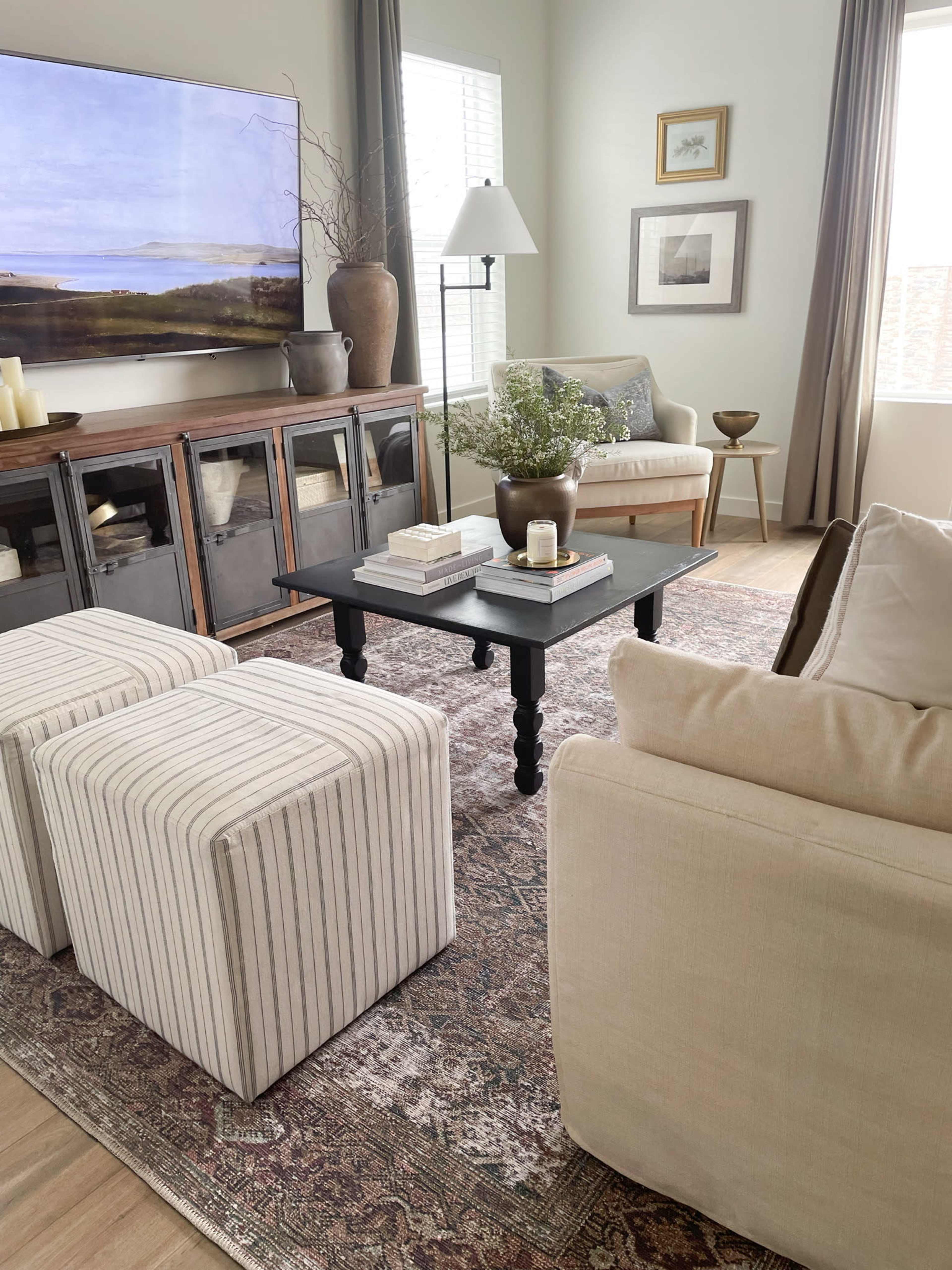 A cozy living room with a beige sofa, a striped accent chair, a wooden media console, and a black coffee table adorned with decorative items, all arranged on a patterned area rug.
