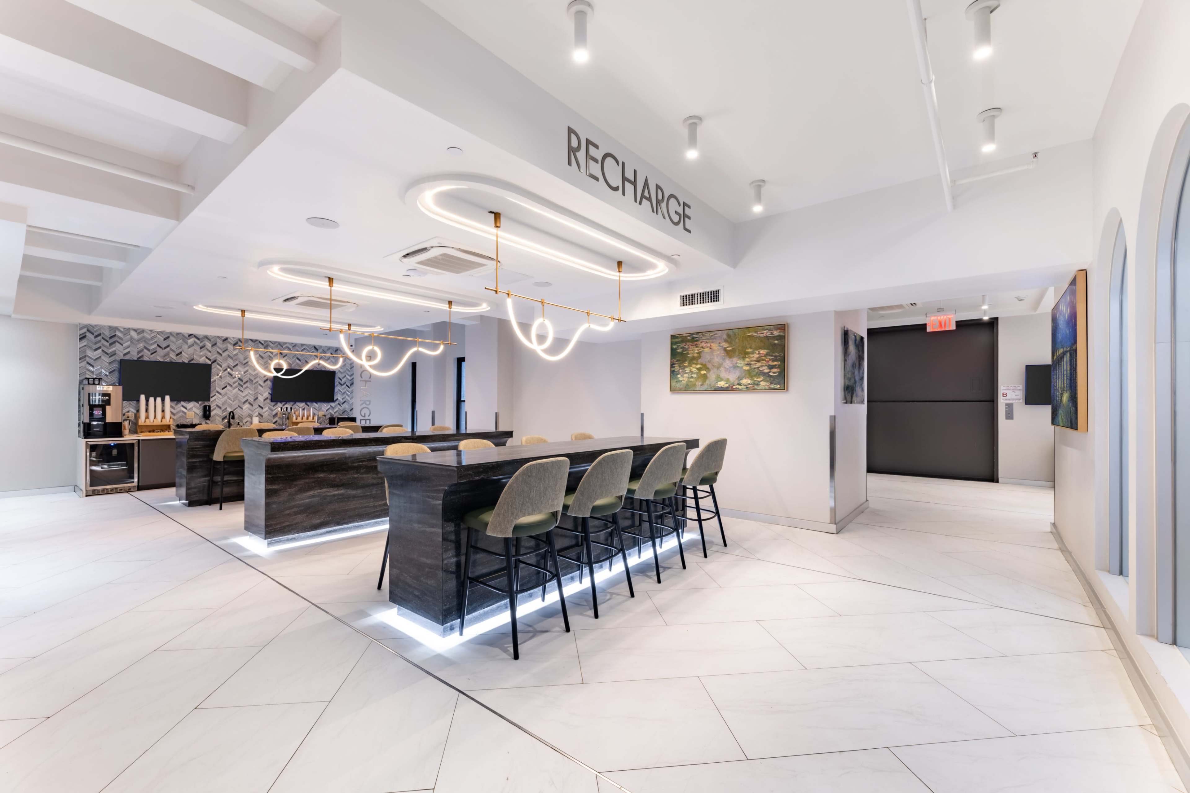 The image shows a modern, well-lit lounge area with a sleek bar, featuring a unique light fixture and minimalist decor in a contemporary design.