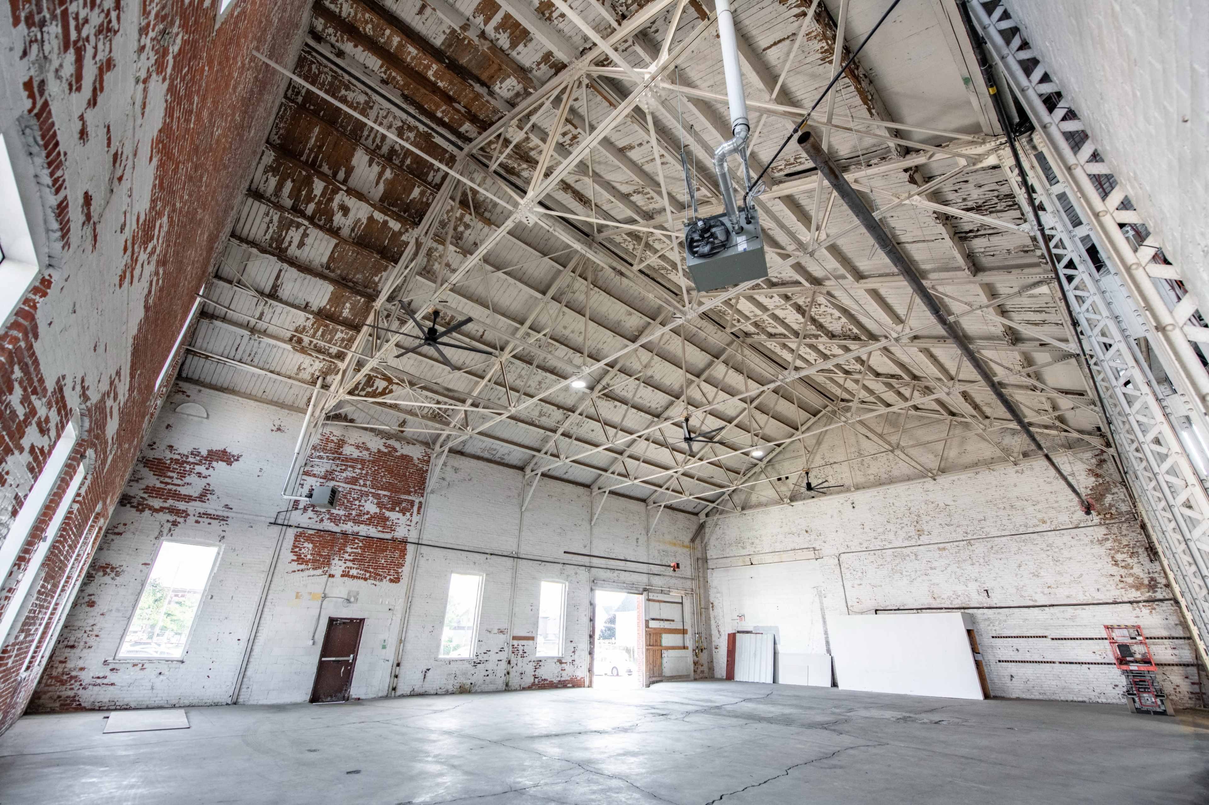 A spacious industrial room with a high ceiling, exposed brick walls, and large windows.