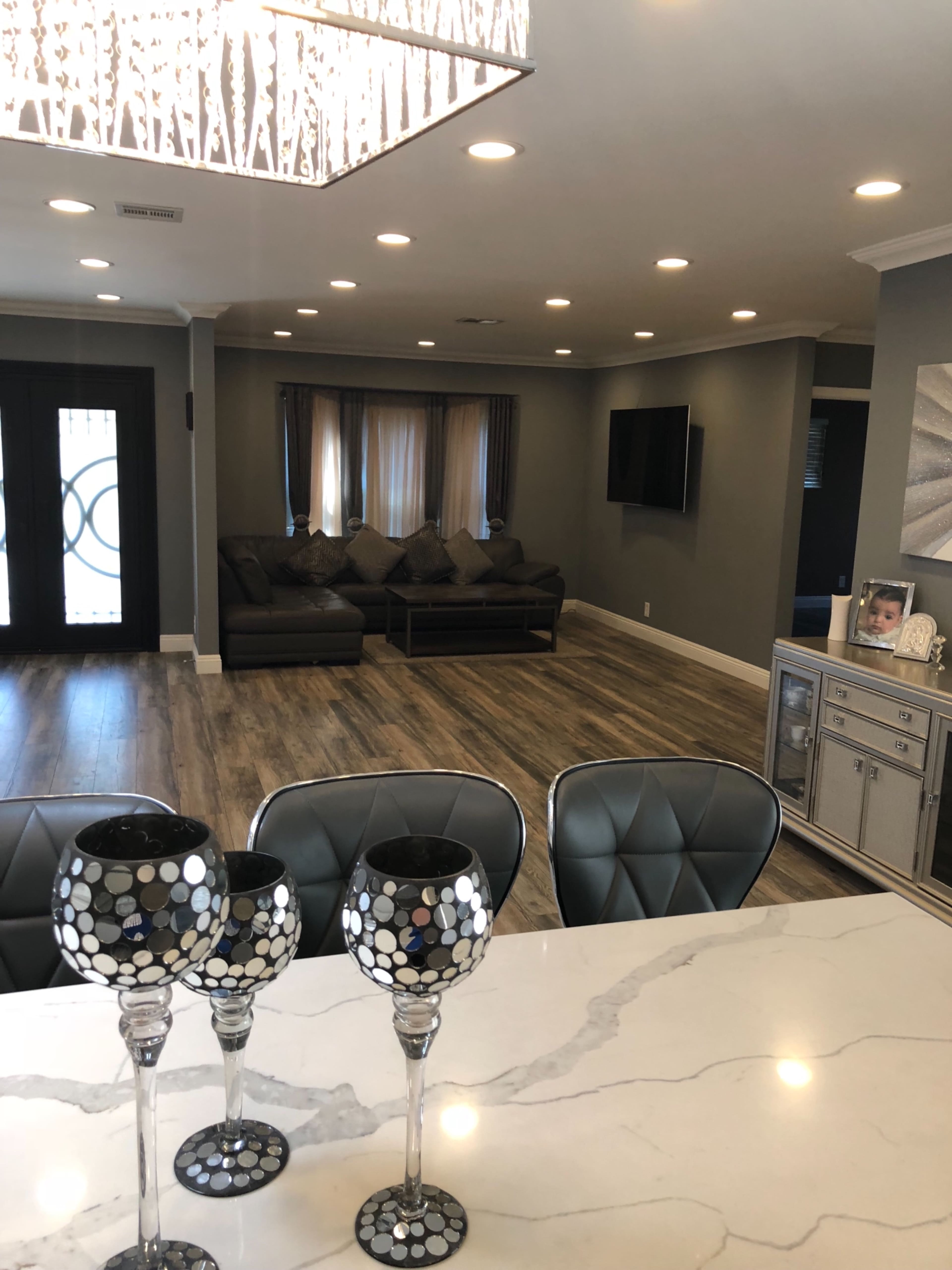 A modern living space with a sectional couch, a television mounted on the wall, and a marble countertop with patterned glasses in the foreground.