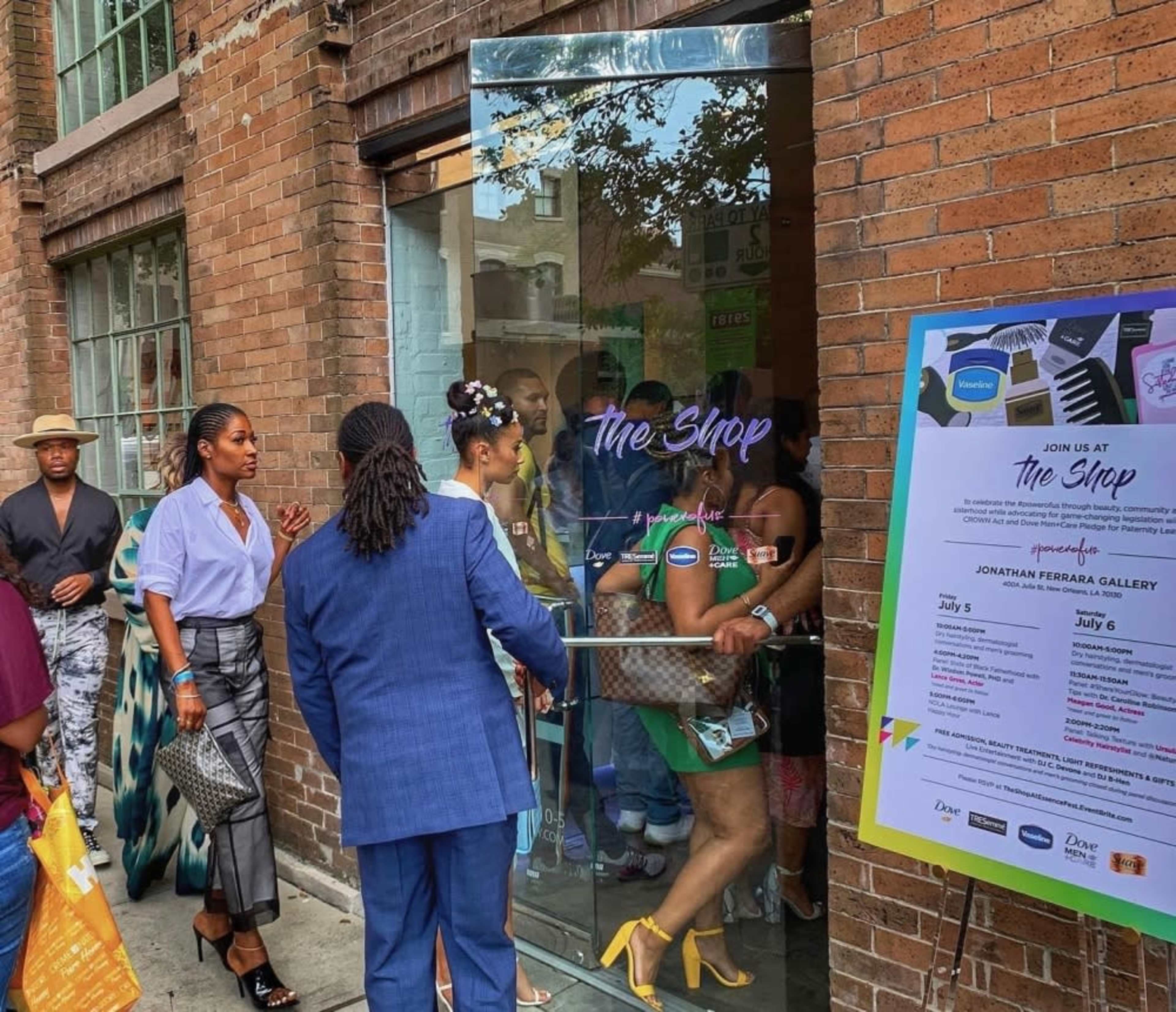 A group of people is entering a storefront labeled "The Shop," with a colorful event sign displayed nearby.