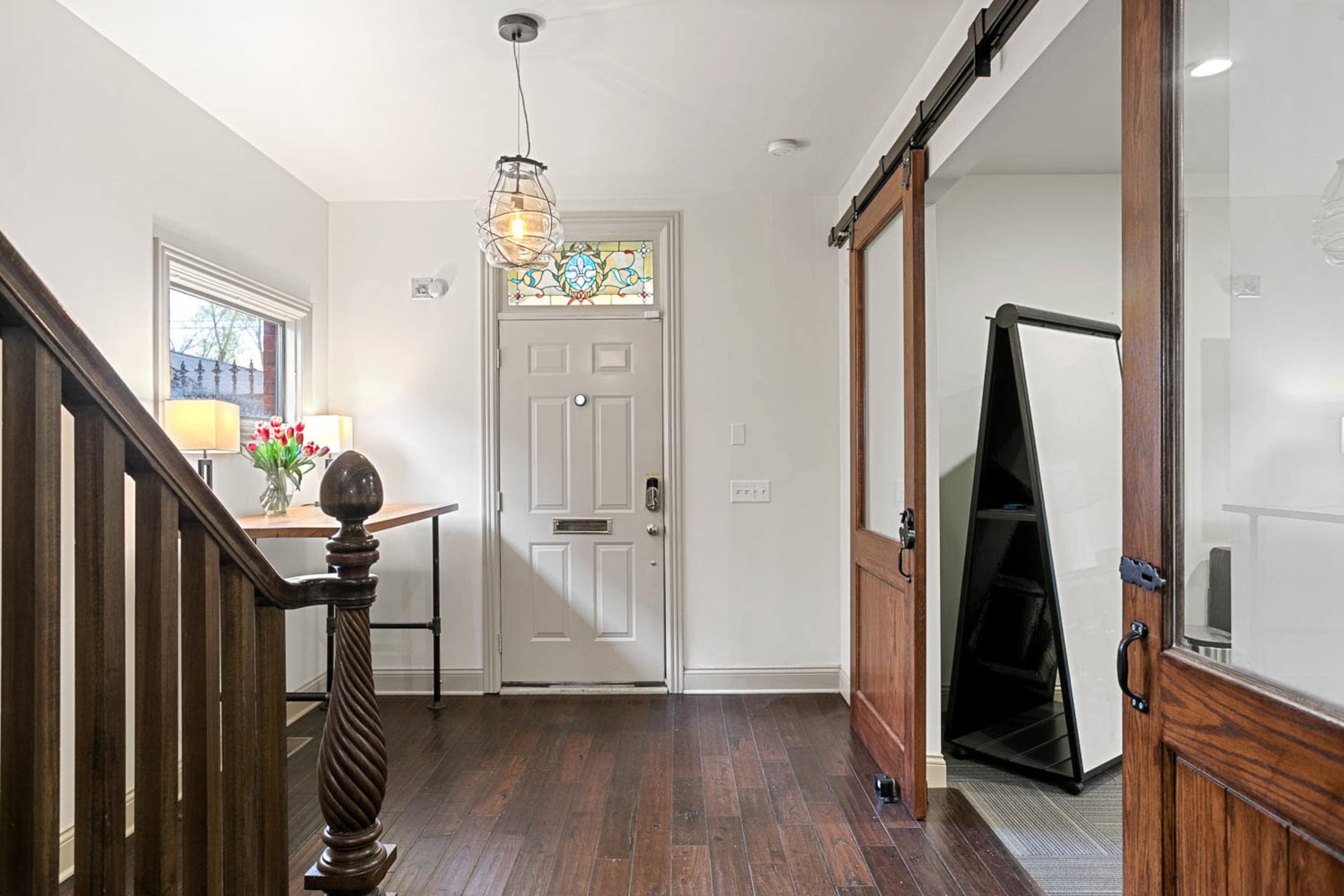 A well-lit entryway featuring a decorative door with a stained glass window, a wooden staircase, and a large mirror near the entrance.