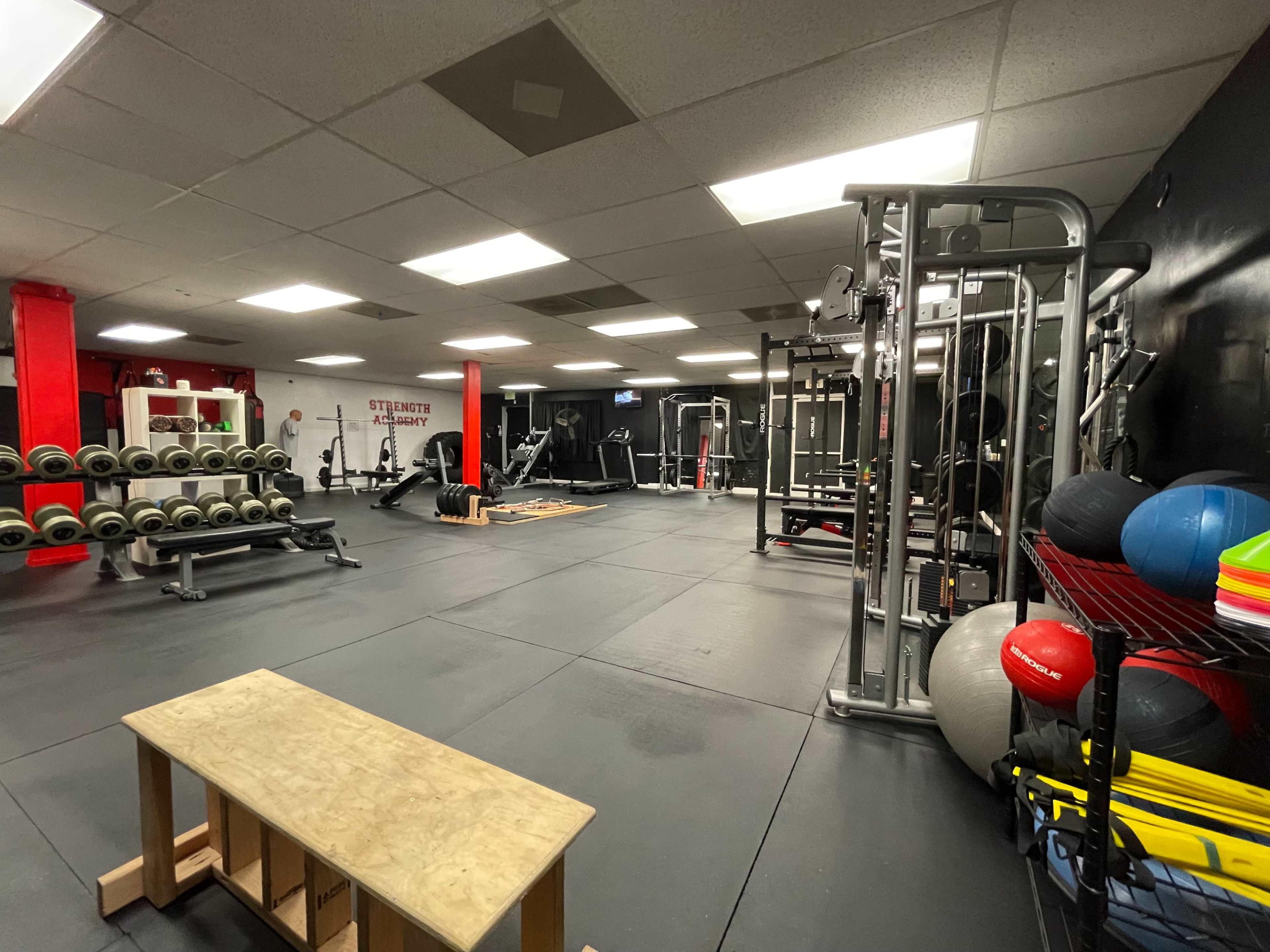 A spacious gym with various weightlifting equipment, exercise mats, and fitness accessories organized neatly in a dark-toned room.