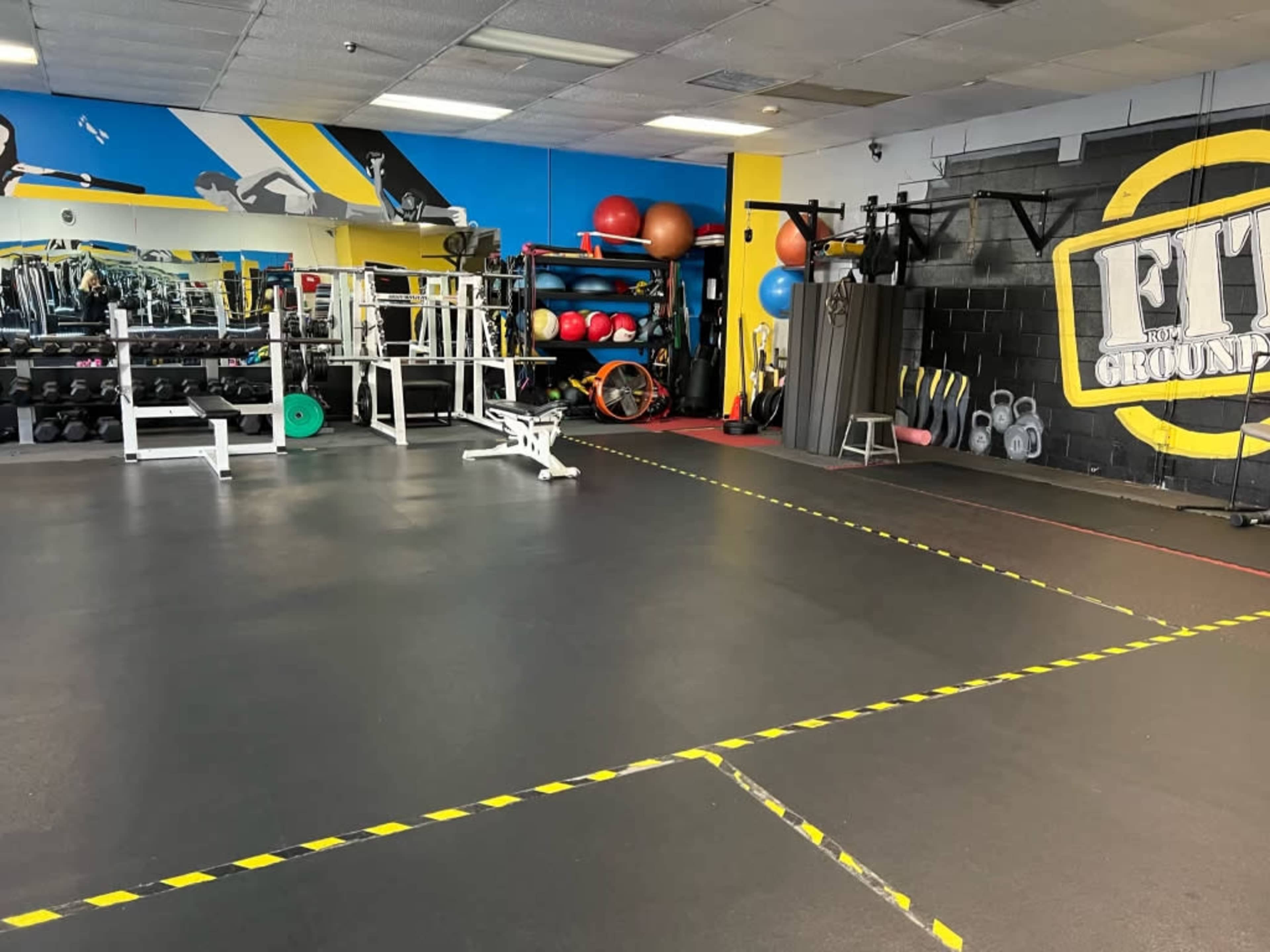 A gym interior featuring various weight training equipment, exercise balls, and marked areas on the floor.
