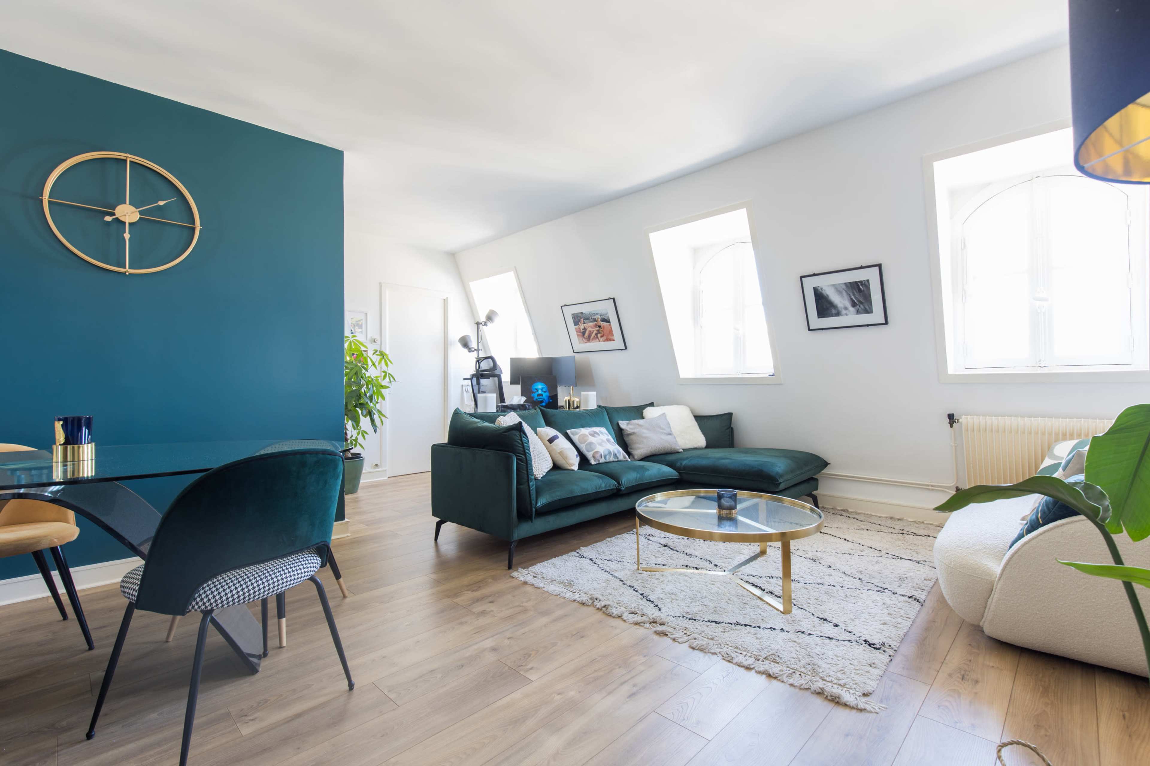 A modern living room features a green accent wall, a comfortable sofa, a glass coffee table, and large windows that allow natural light to fill the space.