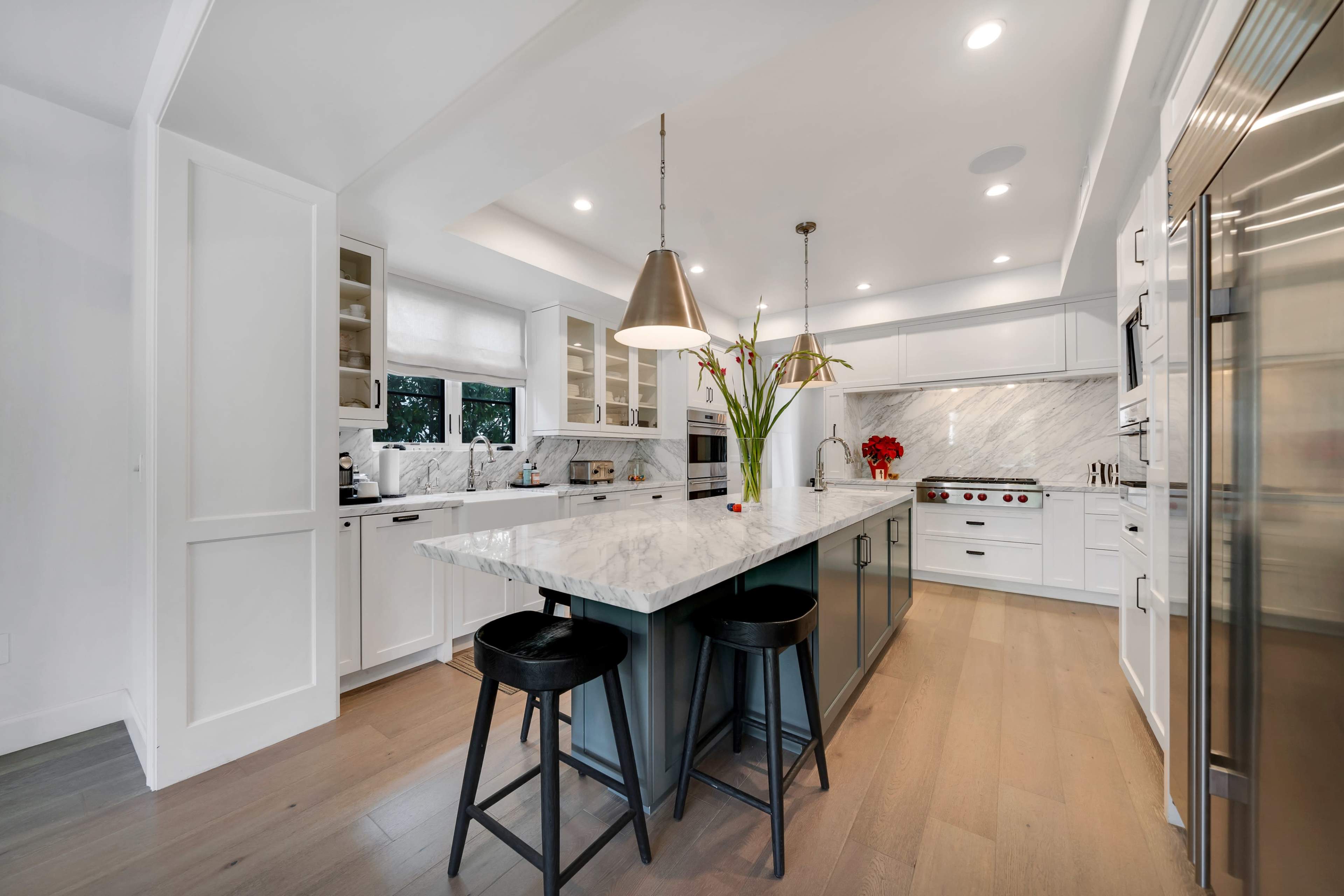 A modern kitchen features a large marble island with bar stools, sleek cabinetry, and high-end appliances.