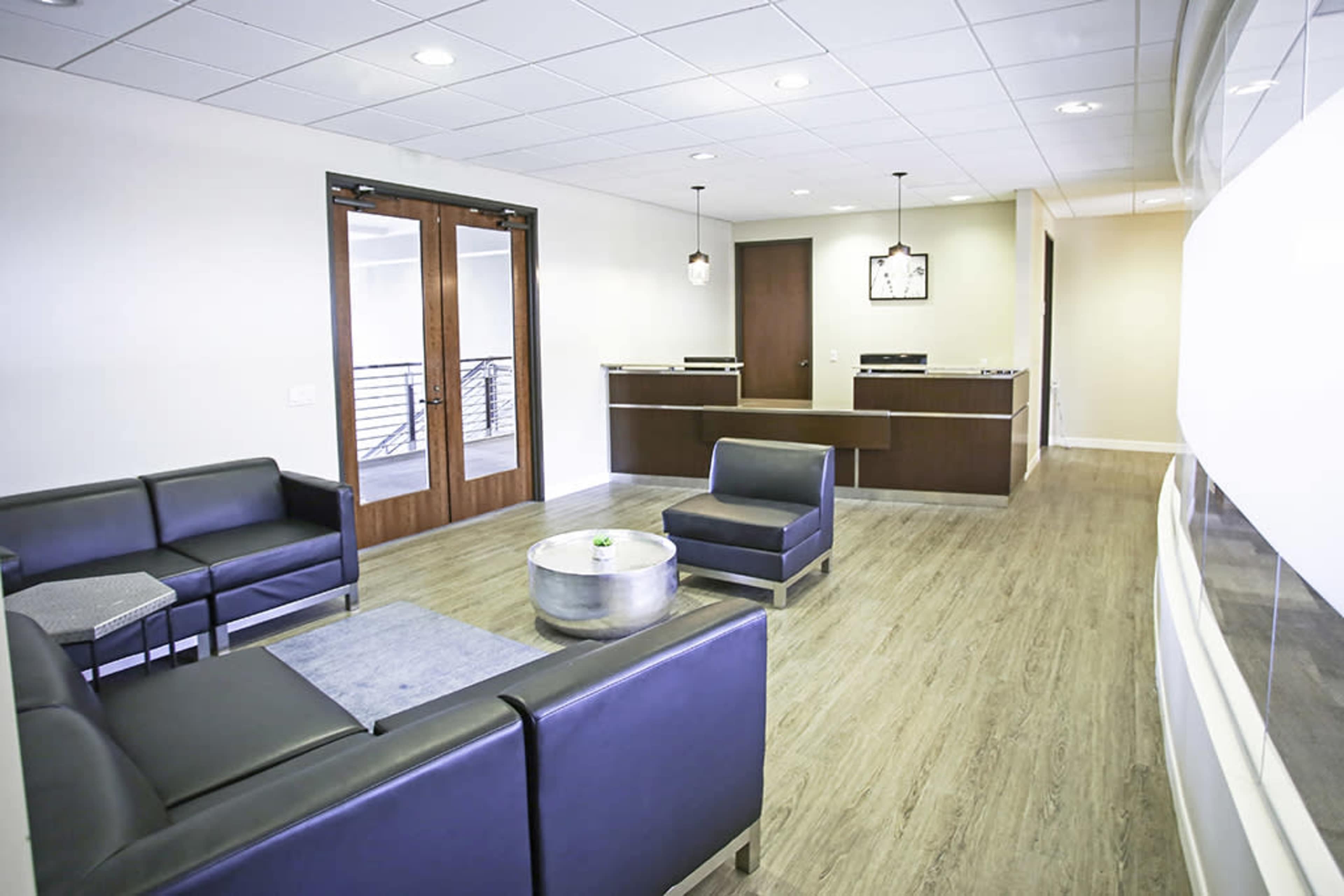 A modern reception area with dark leather seating, a low table, and a front desk in the background.