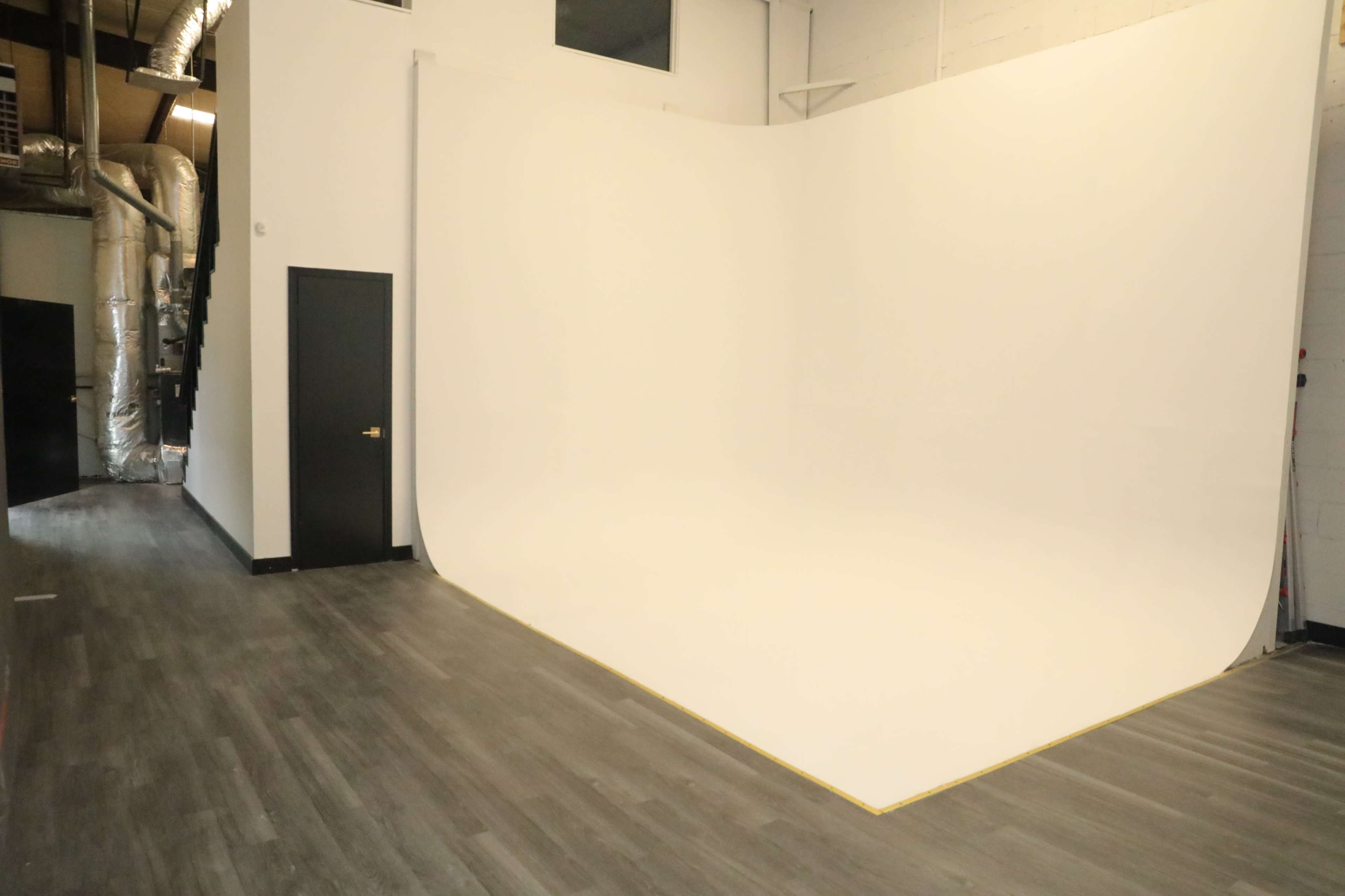 A spacious photo studio with a curved white backdrop and wooden flooring.