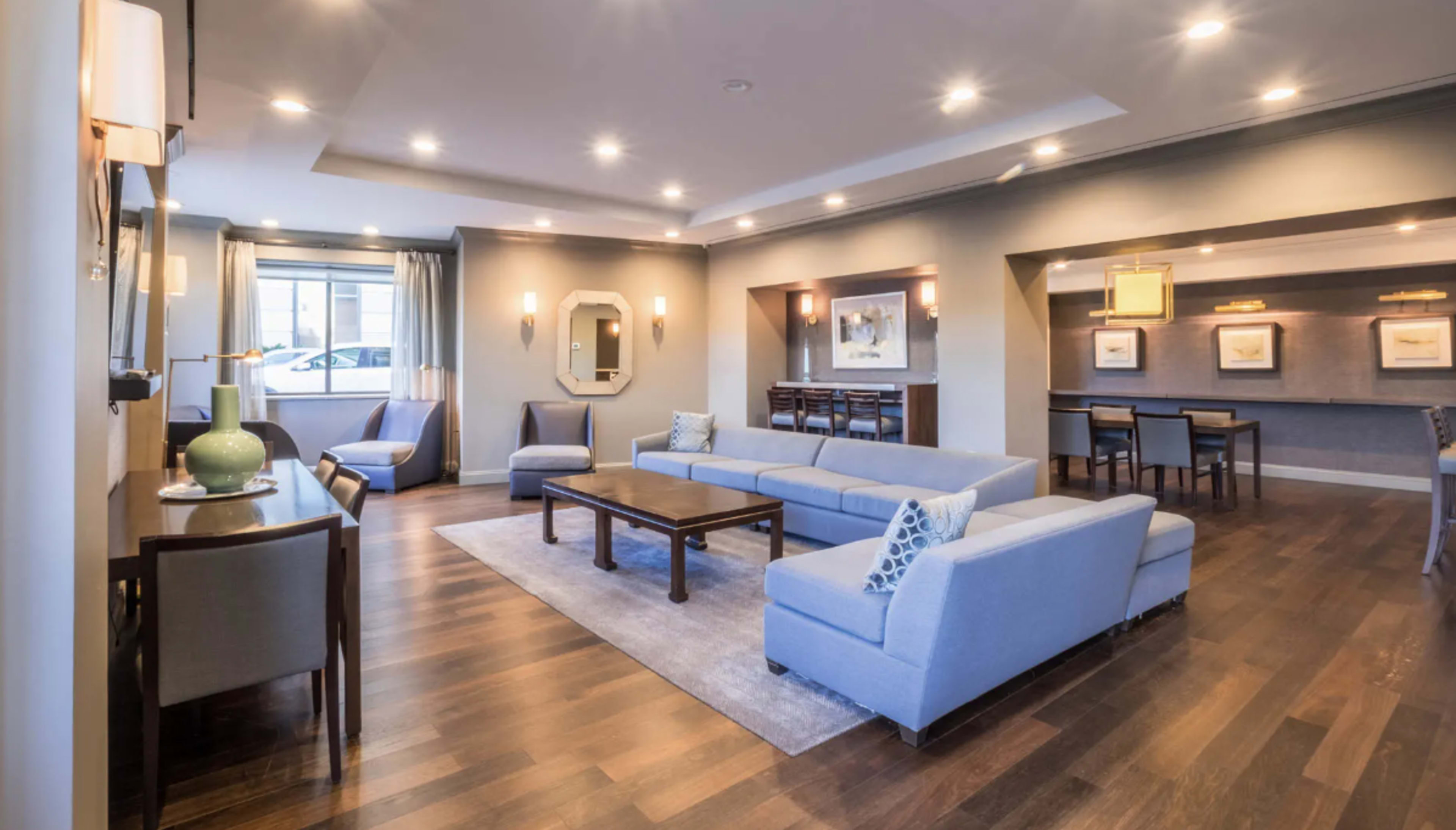 A modern living room with light blue furniture, hardwood floors, and a dining area in the background.