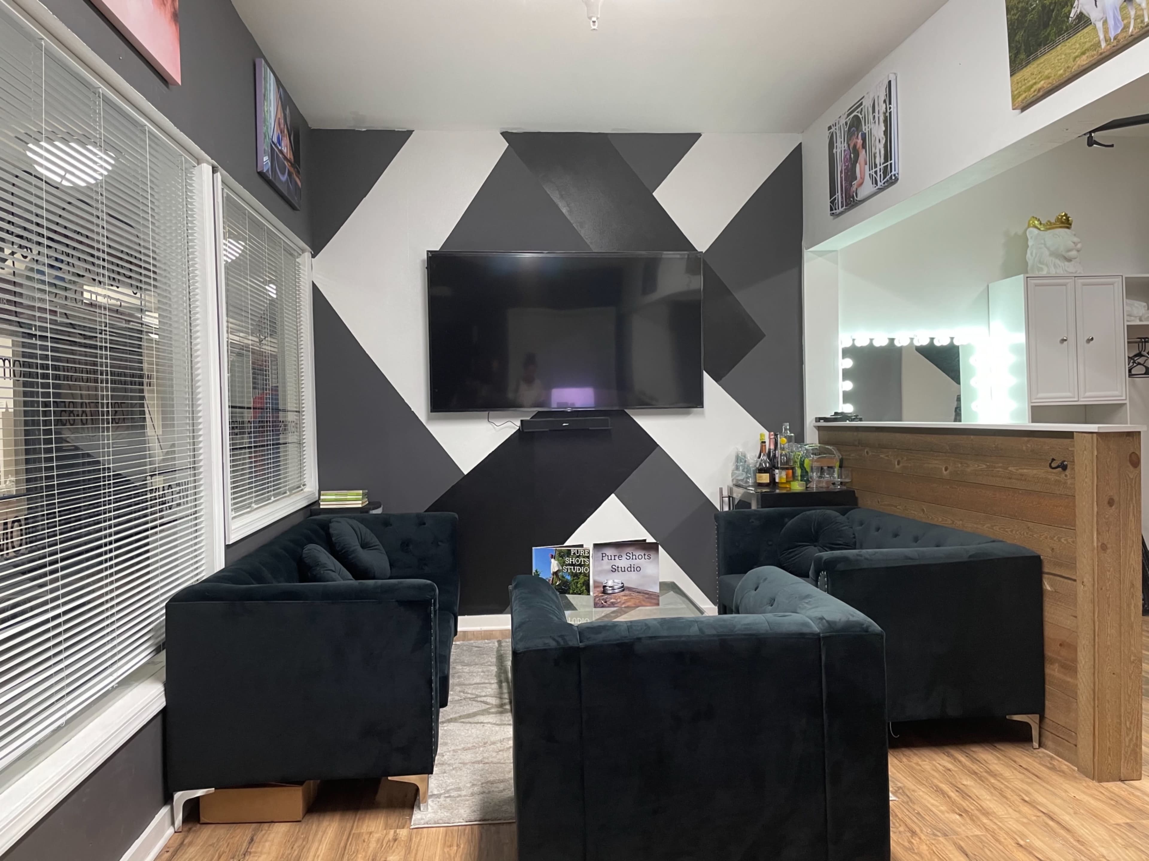 A modern living room with dark-colored sofas arranged around a central area, featuring a large flat-screen TV mounted on the wall and a bar cart in the corner.