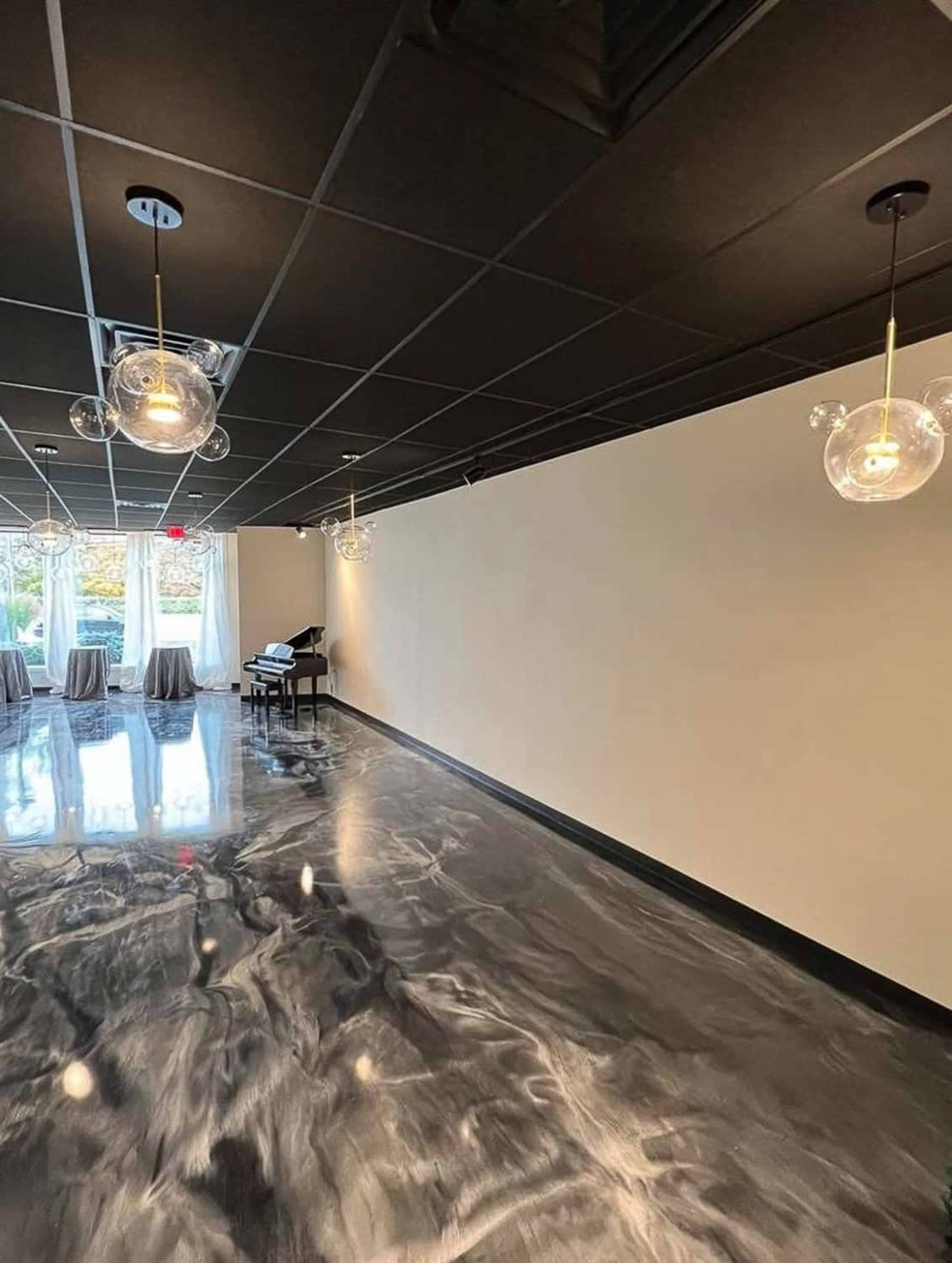 The image shows a spacious room with a polished floor, modern pendant lights hanging from the ceiling, and large windows letting in natural light.