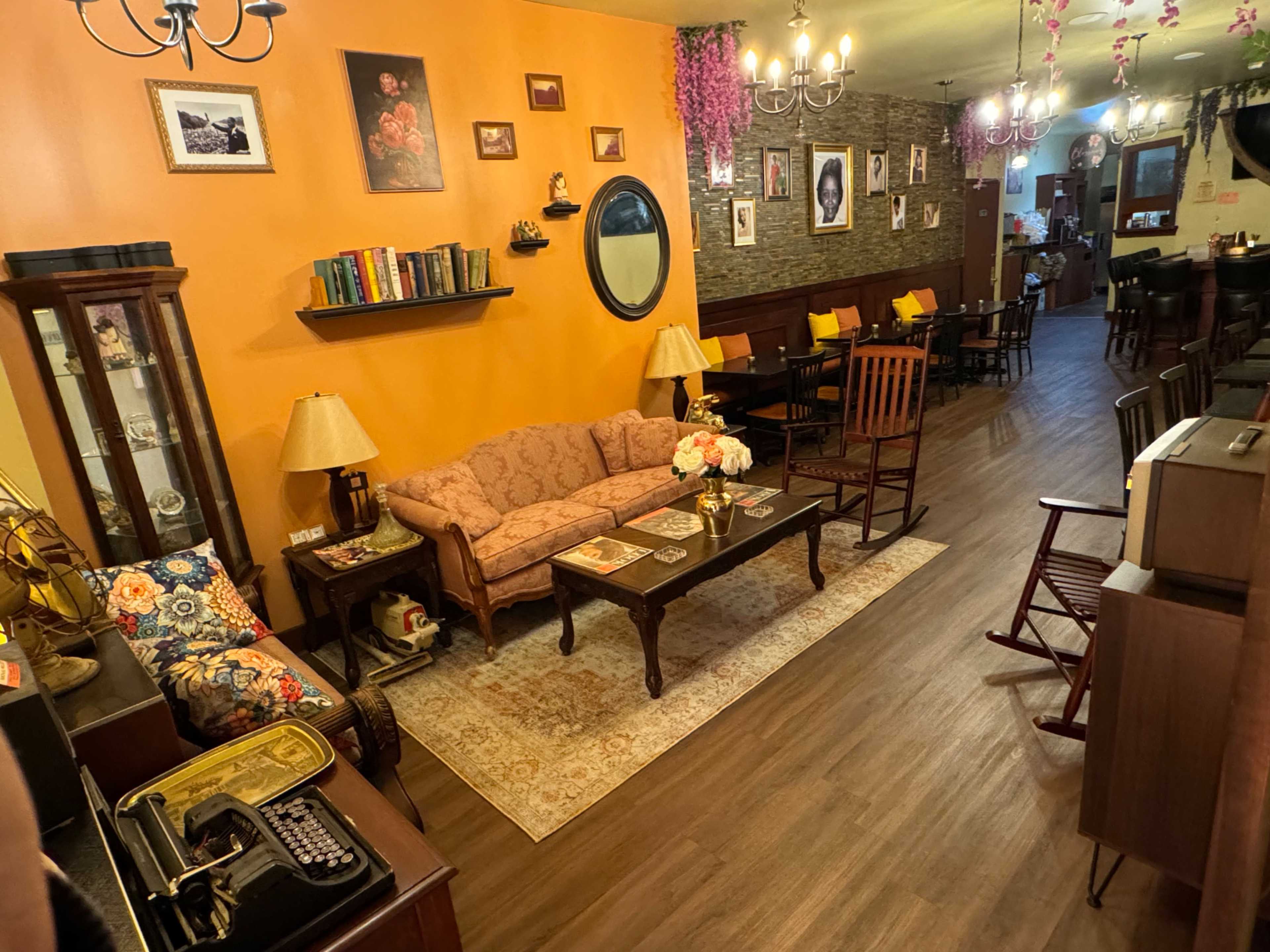 The image shows a cozy café interior with orange walls, wooden furniture, and various decorations, including bookshelves and photographs.